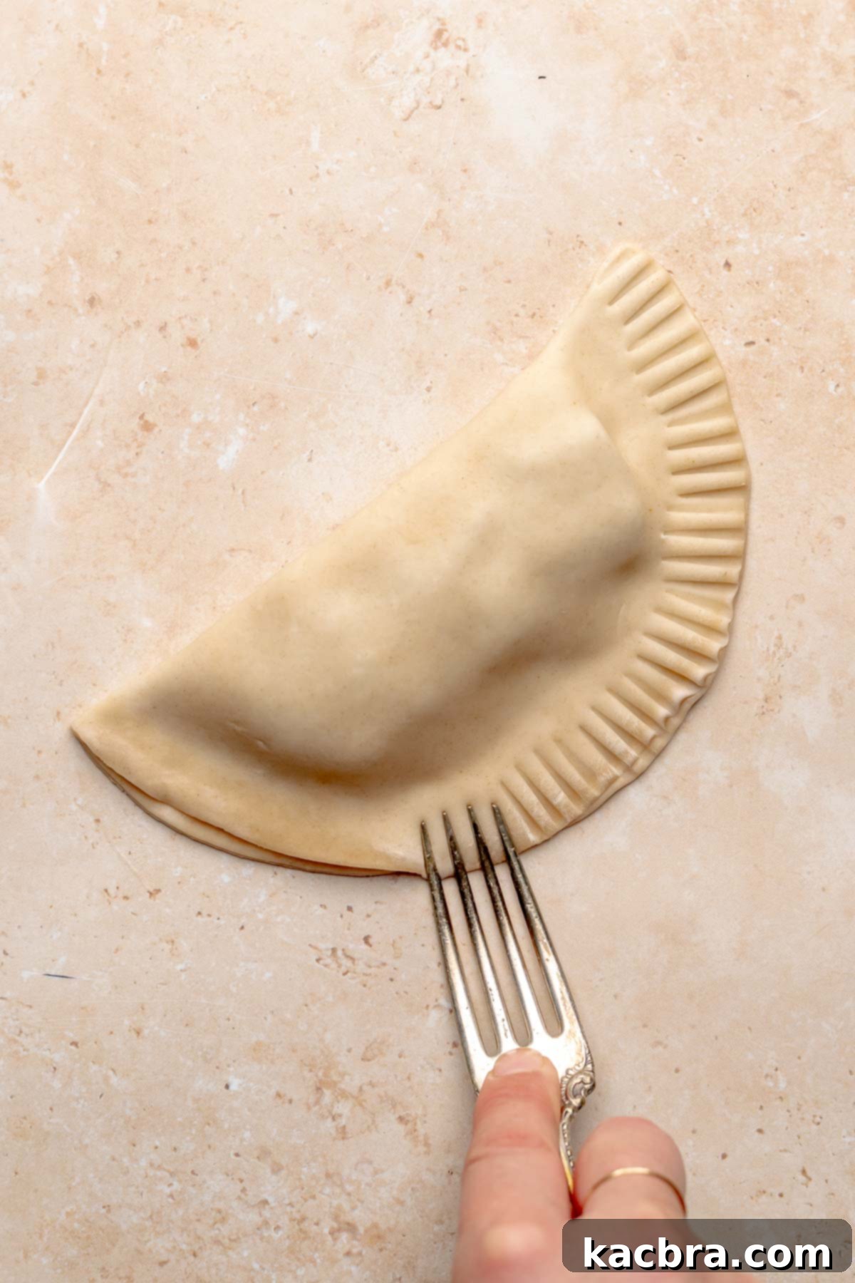 A fork crimps the edge of a folded empanada to seal it.