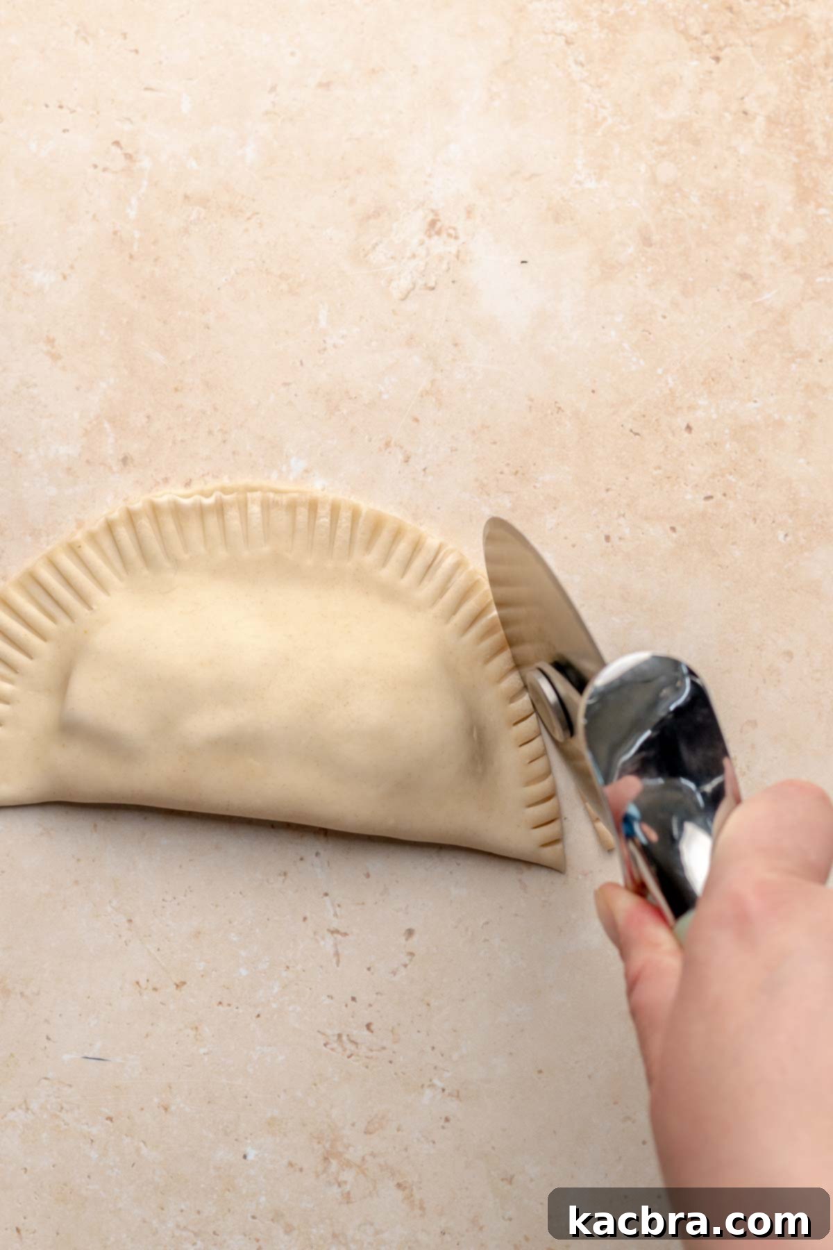 A pizza cutter trims the edges of an empanada.