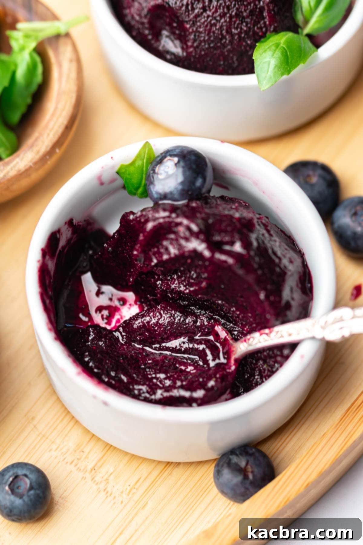 A spoon in a cup of half eaten blueberry sorbet.