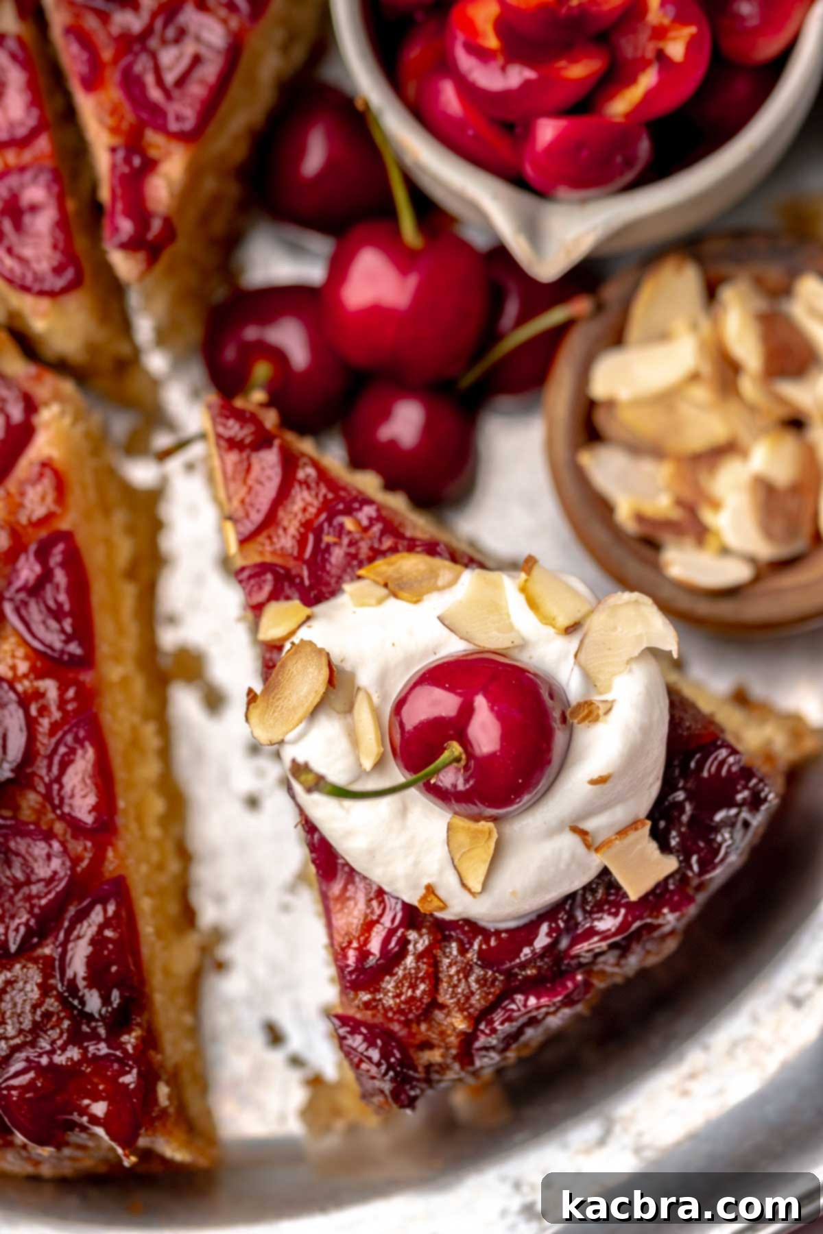 Sliced cherry upside down cake on a platter with a dollop of whipped cream on top, ready to serve.
