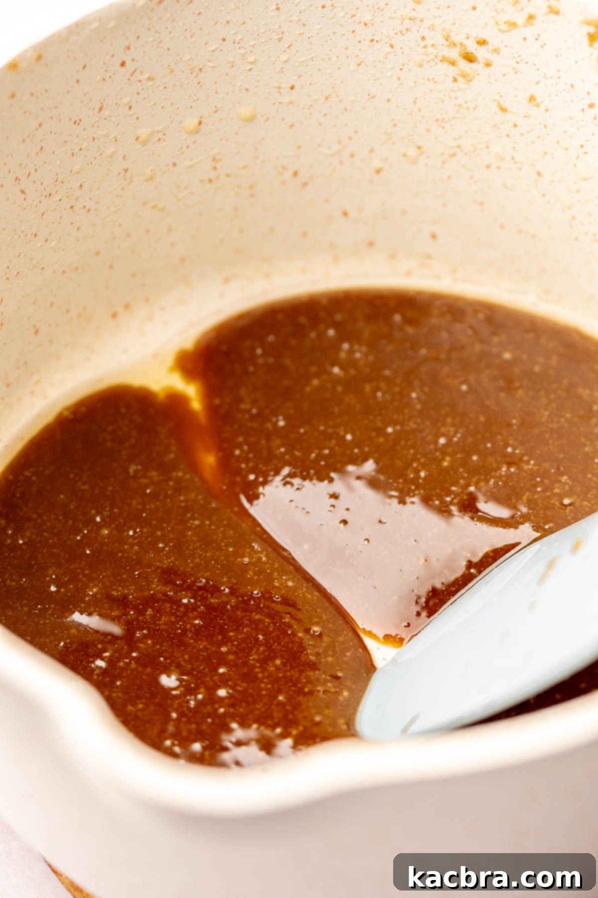 A spatula runs through melted caramel in a pot, demonstrating the first step.