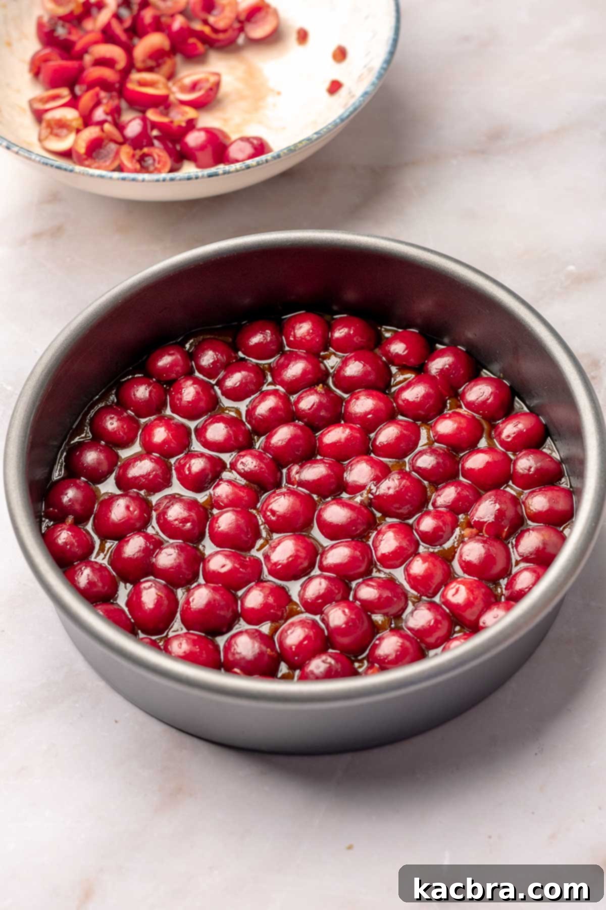Fresh cherry halves nested into caramel in a cake pan, cut side down.