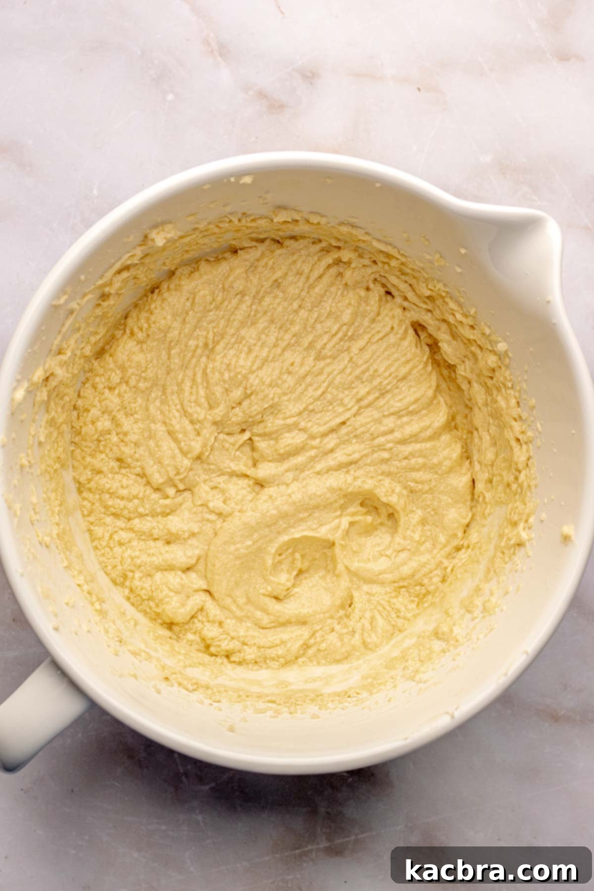 Whisked eggs and extracts being incorporated into the creamed butter and sugar mixture.