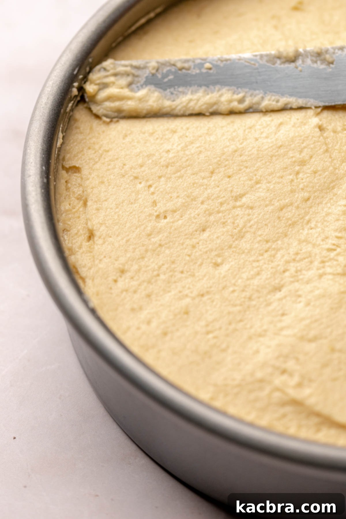 A spatula spreads cake batter evenly over the cherries in the prepared cake pan.