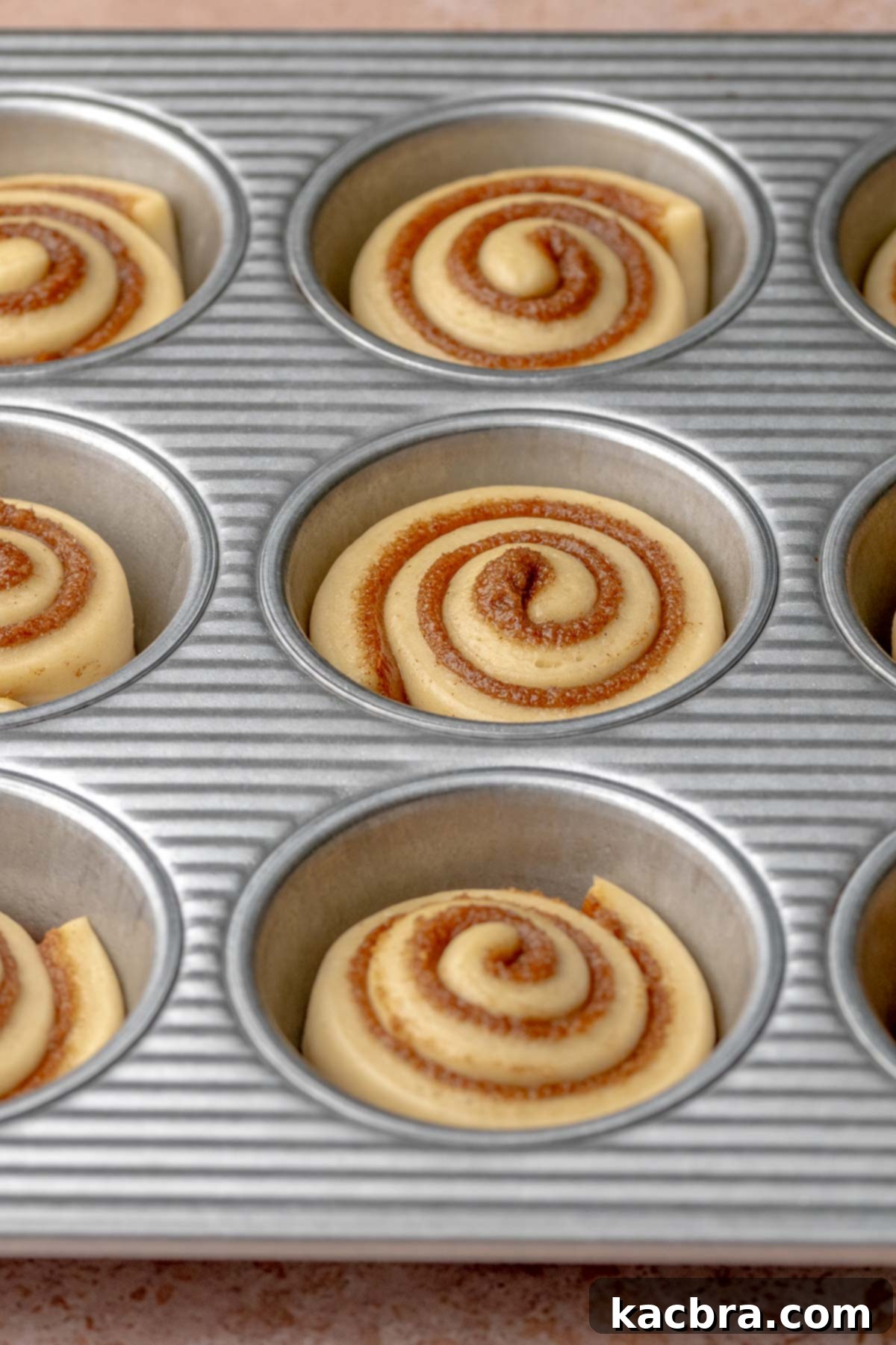 Risen, pre-baked mini cinnamon rolls in a muffin tin.