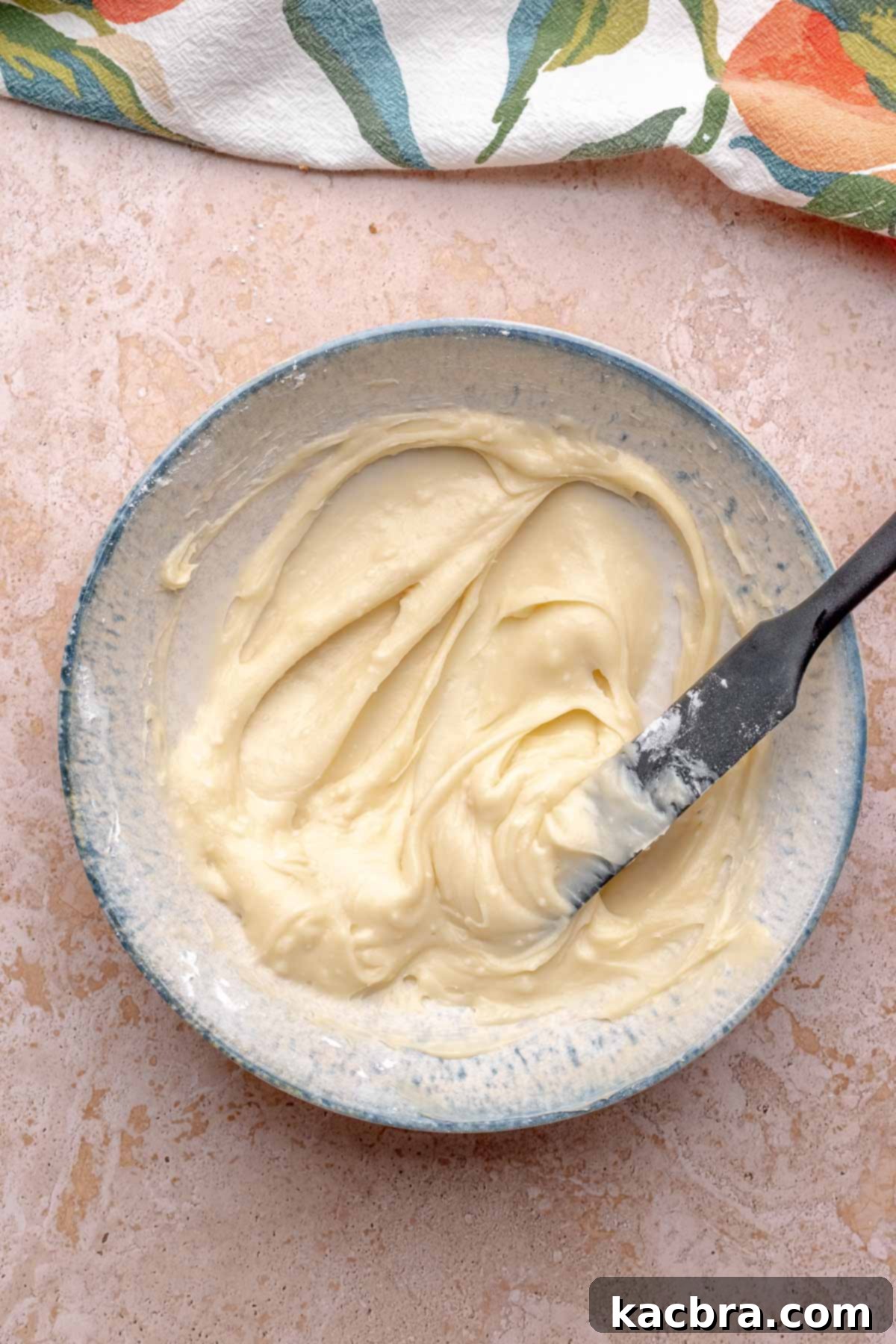A rubber spatula mixes cream cheese frosting in a bowl.