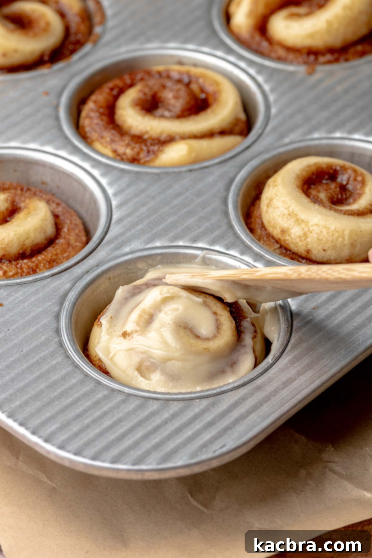 A knife spread cream cheese frosting on top of a mini cinnamon roll.