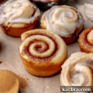 An array of mini cinnamon rolls, half are frosted.