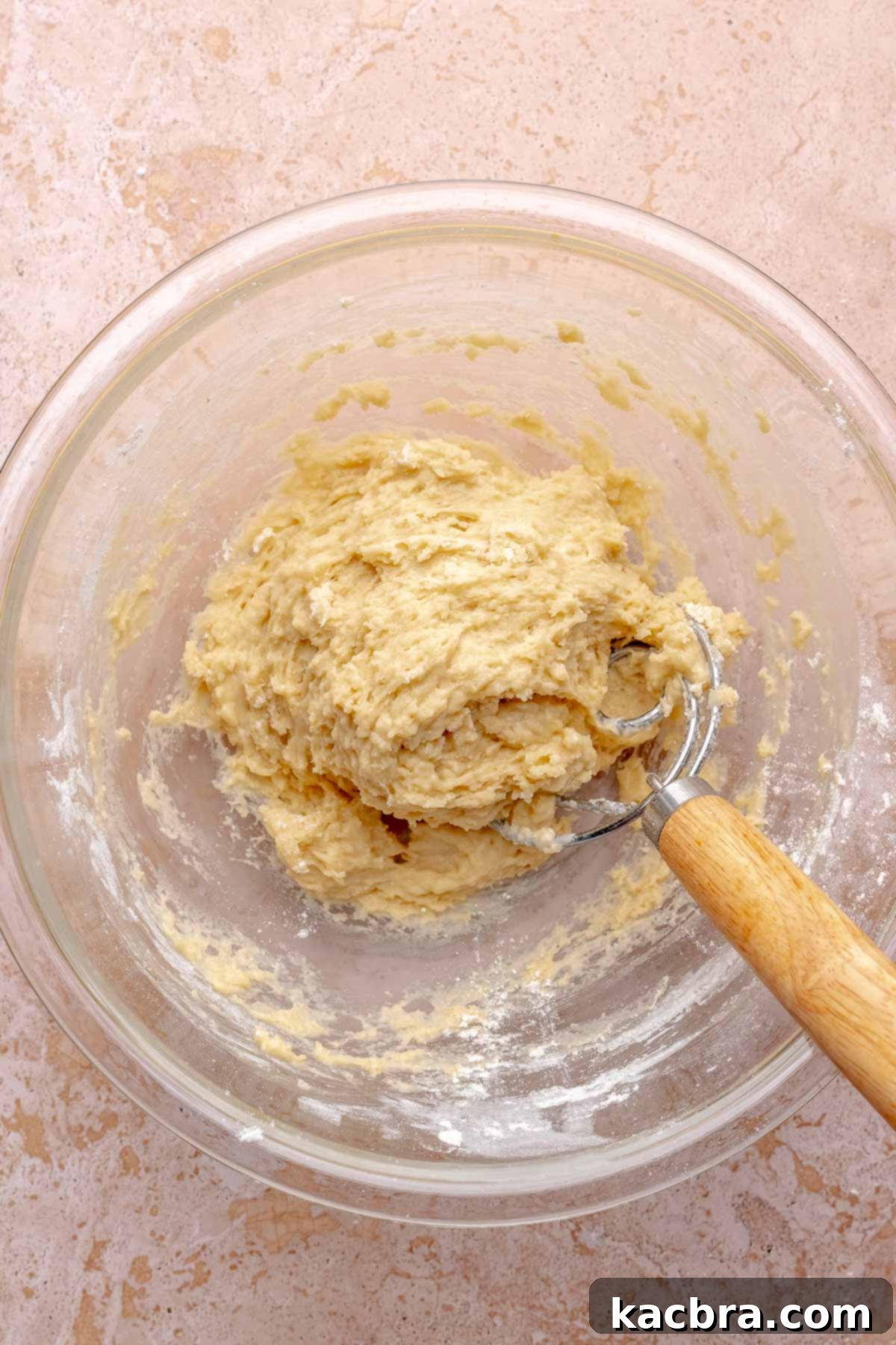 A dough whisk mixes cinnamon roll dough in a bowl.