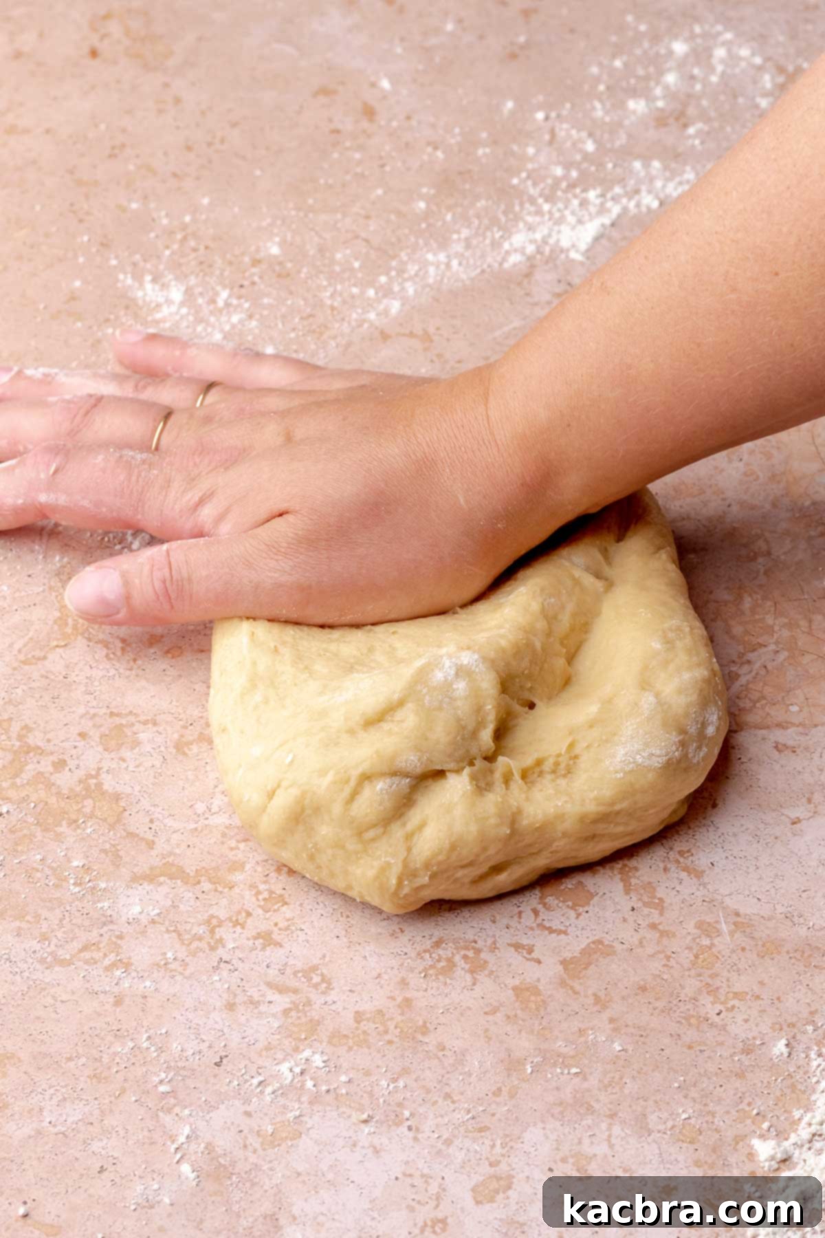 A hand kneads cinnamon roll dough.