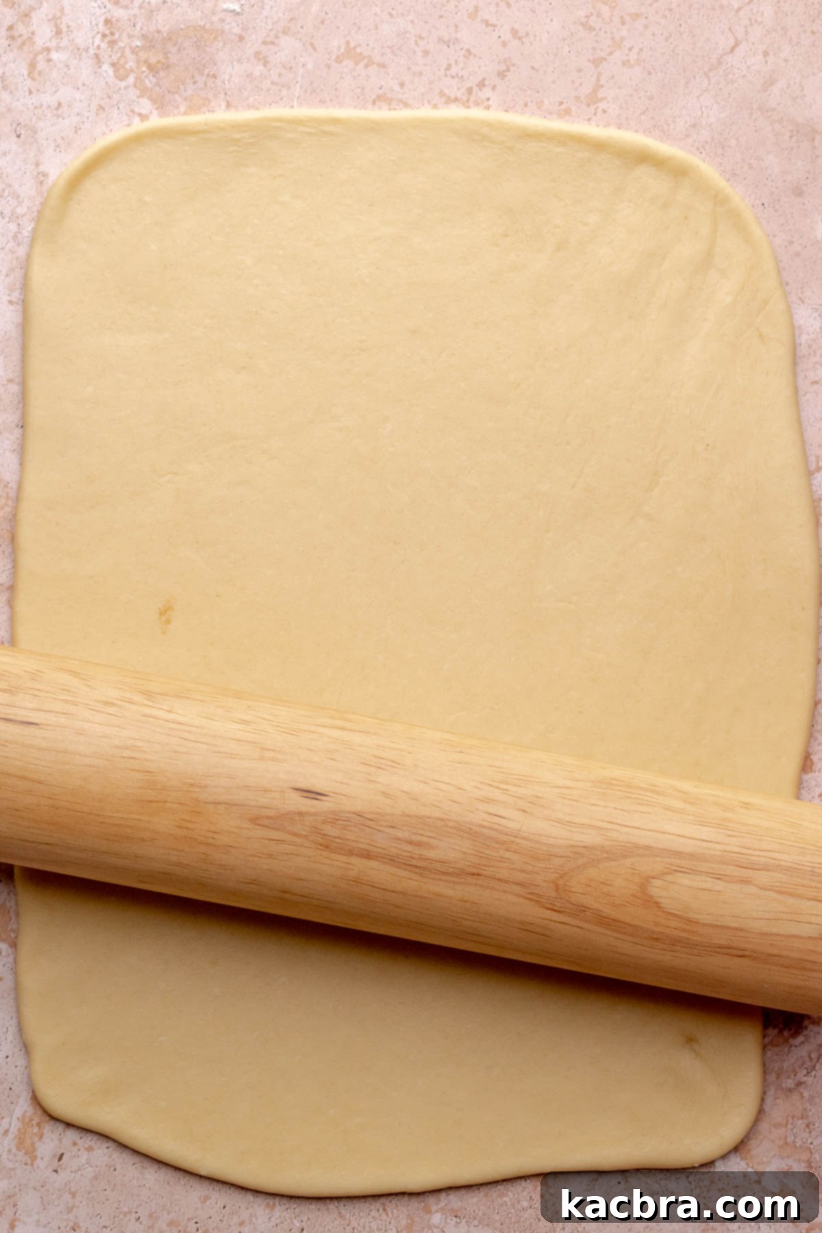 A rolling pin rolling out a rectangle of cinnamon roll dough.
