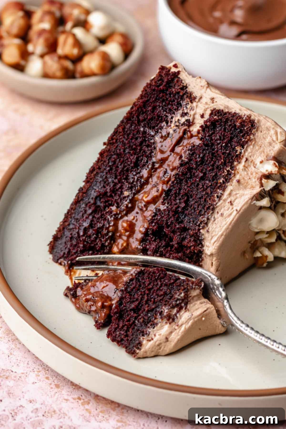 A fork cuts into a slice of chocolate hazelnut cake on a plate, showcasing its moist layers and creamy filling.