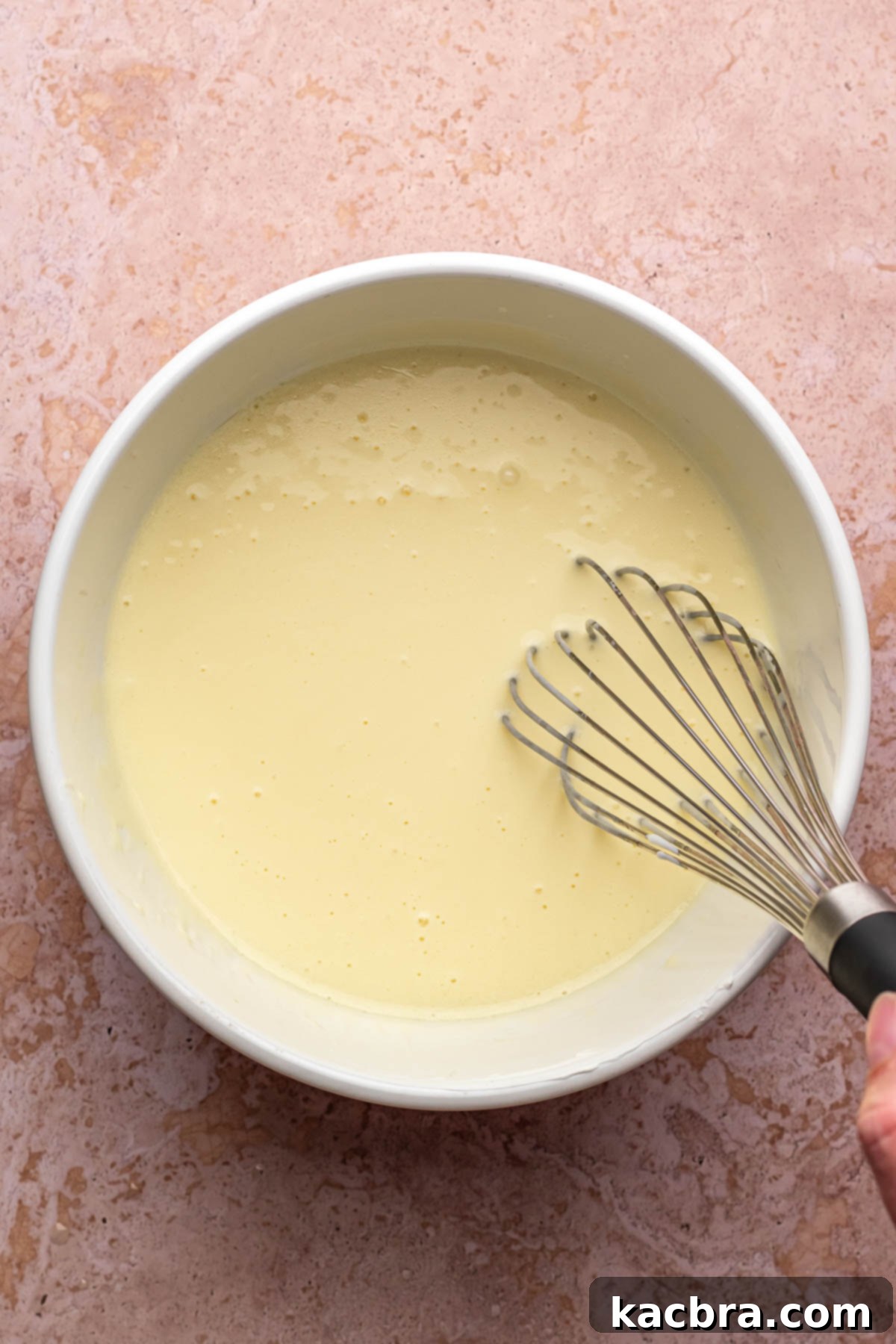 A whisk mixes wet chocolate cake ingredients in a bowl.