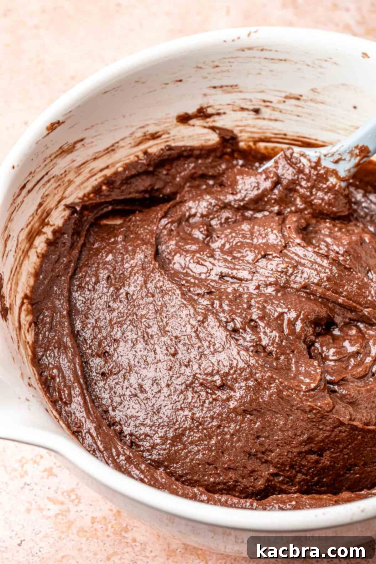 A spatula folds together chocolate cake ingredients in a bowl.