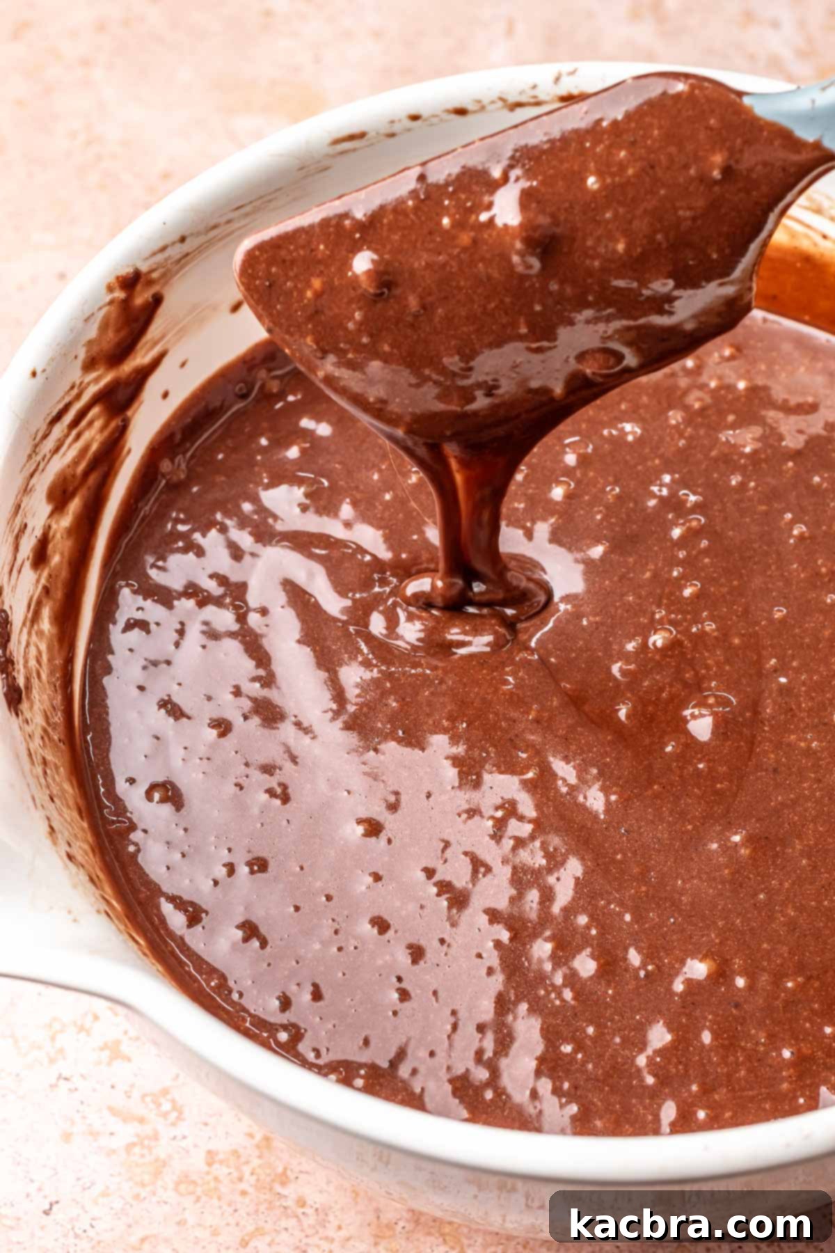 A spatula folds together chocolate cake ingredients in a bowl.
