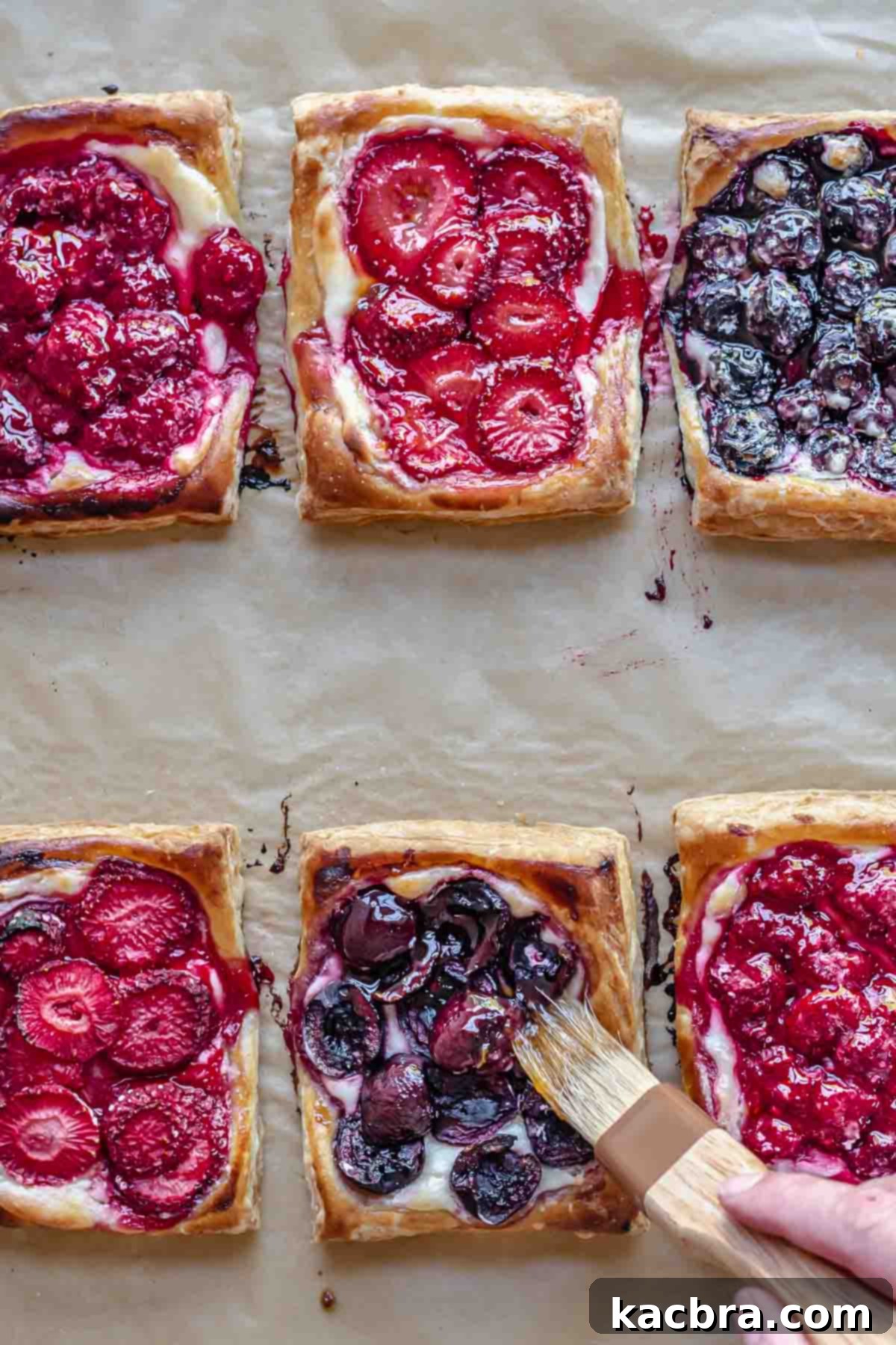 A pastry brush brushes on fruit spread to the baked danish.