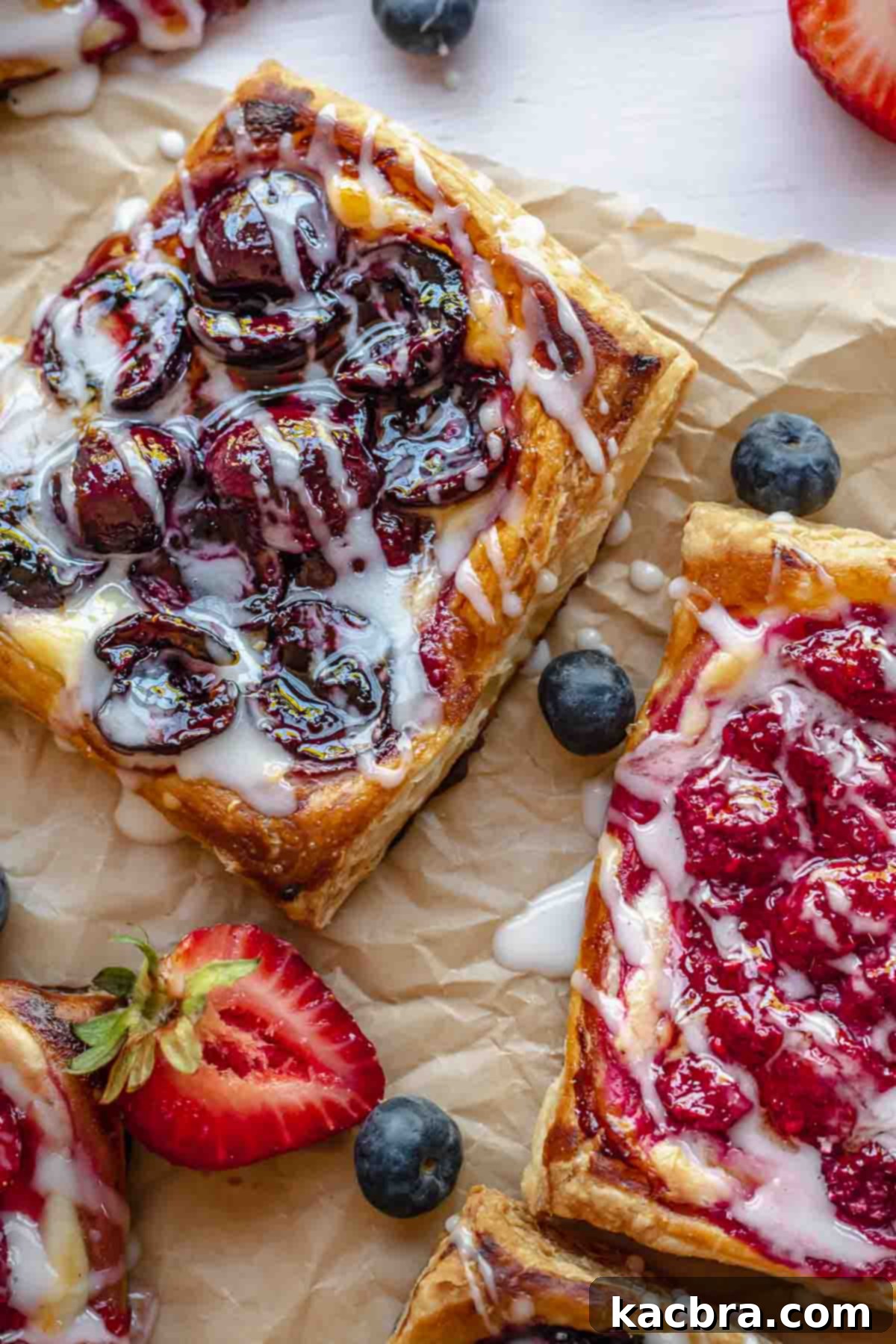 Cherry danish and raspberry cream cheese danish on parchment paper drizzled with icing.