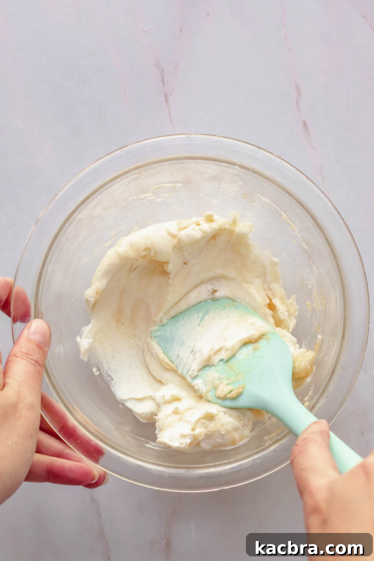 A spatula mixes cream cheese and sugar in a bowl.