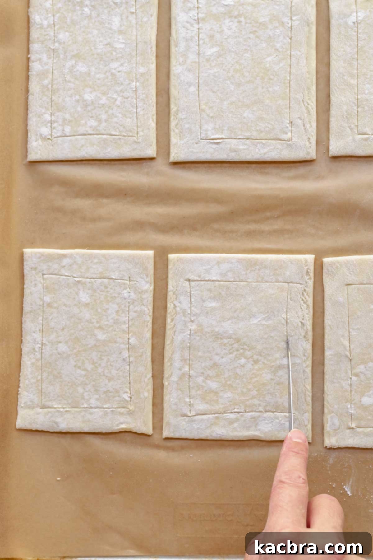 The tip of a knife scoring borders on the puff pastry pieces.