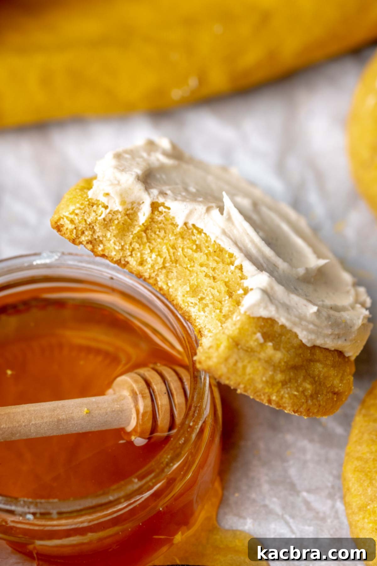 Warm Cornbread Cookies with Whipped Honey Butter 15 A beautifully frosted cornbread cookie with a bite taken out, resting against a small bowl of golden honey, highlighting its deliciousness.