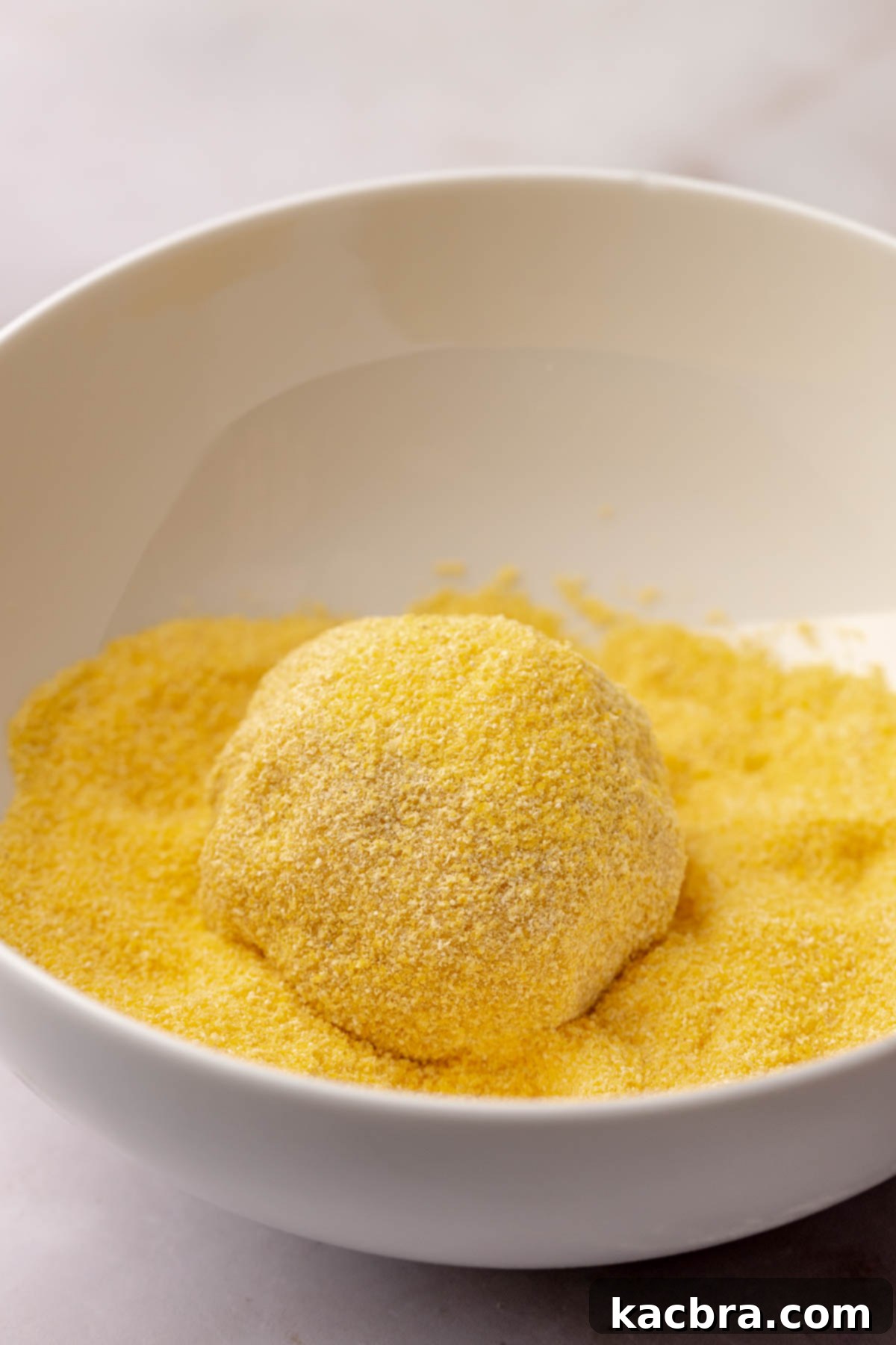 Warm Cornbread Cookies with Whipped Honey Butter 9 A cookie dough ball being rolled in cornmeal, creating a textured coating.