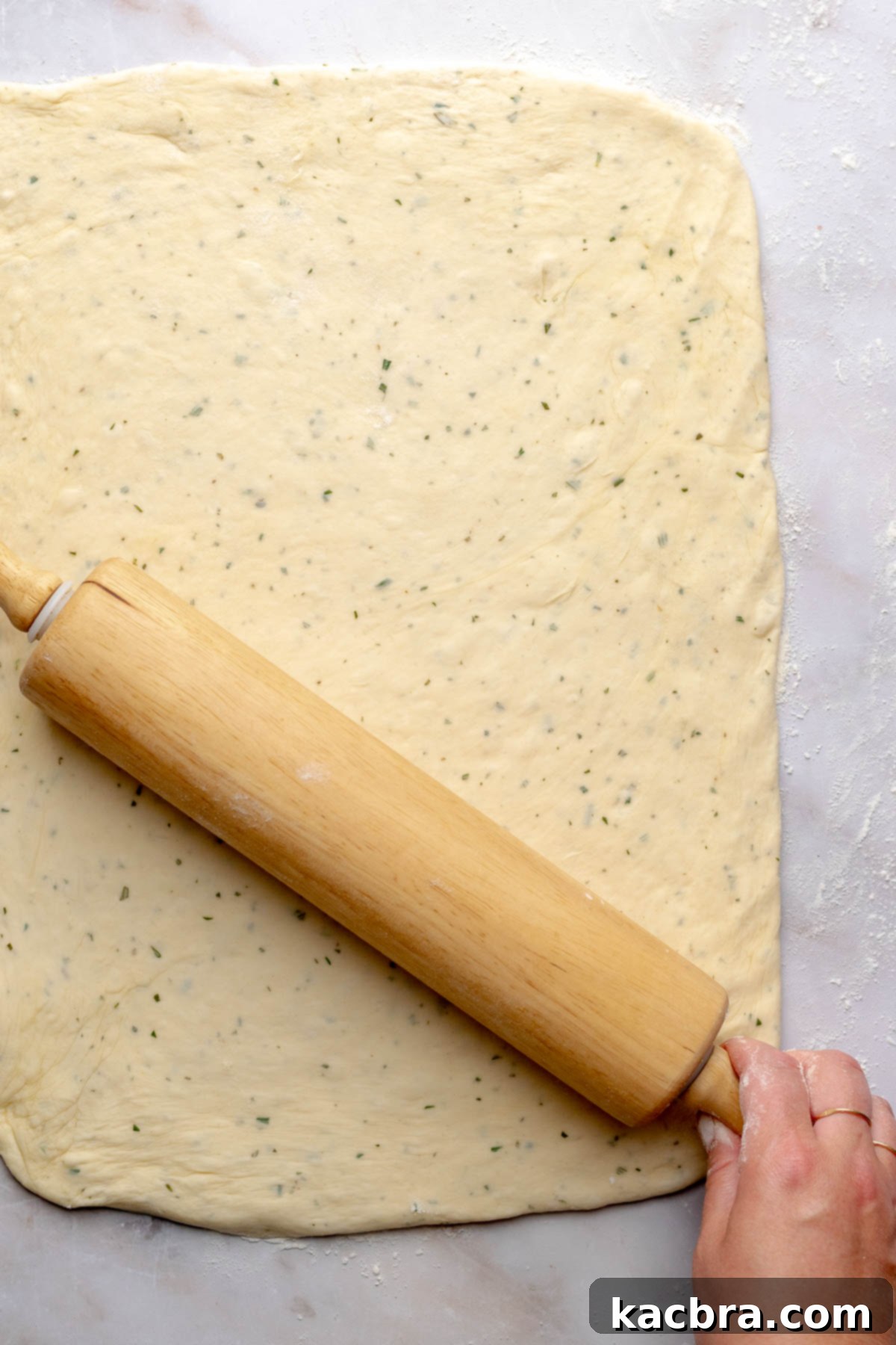 Fluffy Savory Rolls with Golden Hollandaise 11 A rolling pin extends savory cinnamon roll dough into a rectangular shape.
