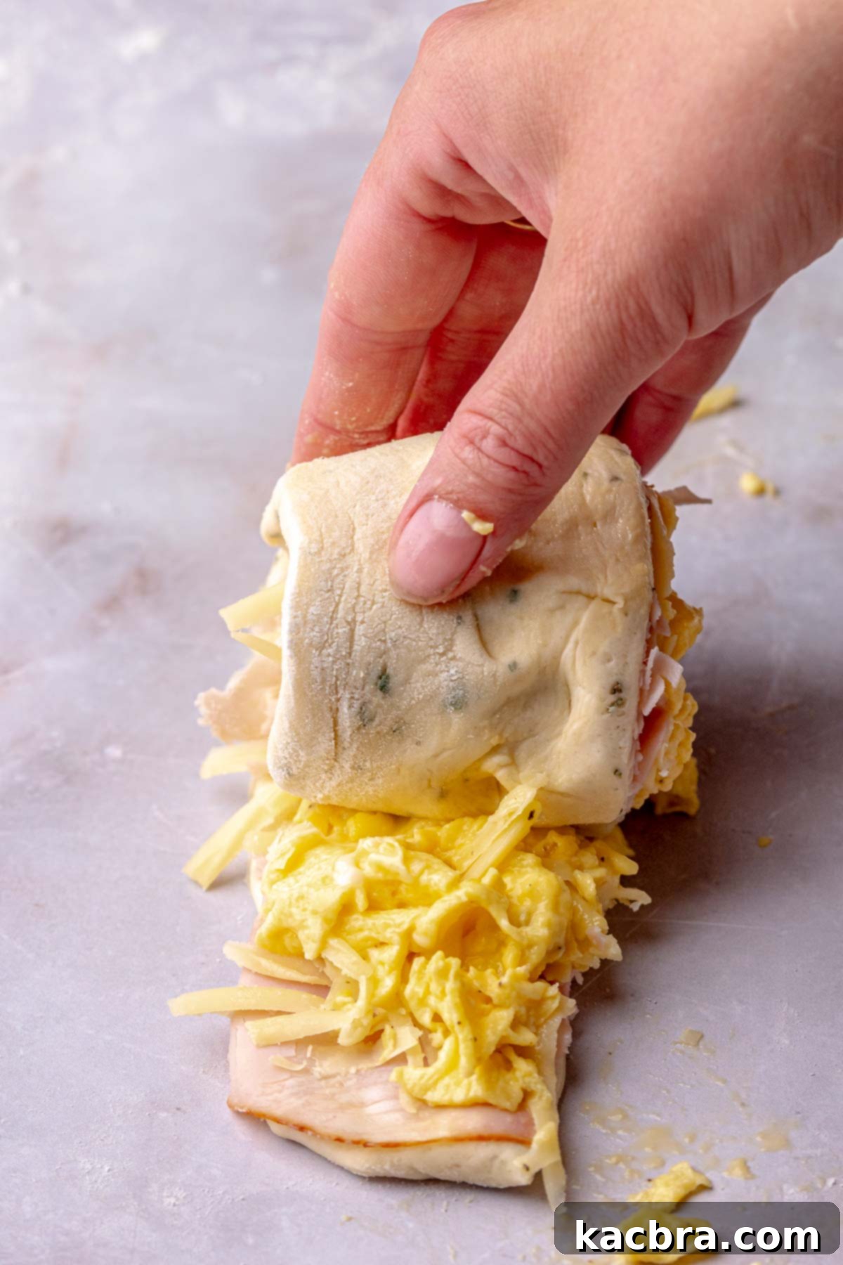 Fluffy Savory Rolls with Golden Hollandaise 13 A hand carefully rolls up a strip of savory cinnamon roll dough with filling.