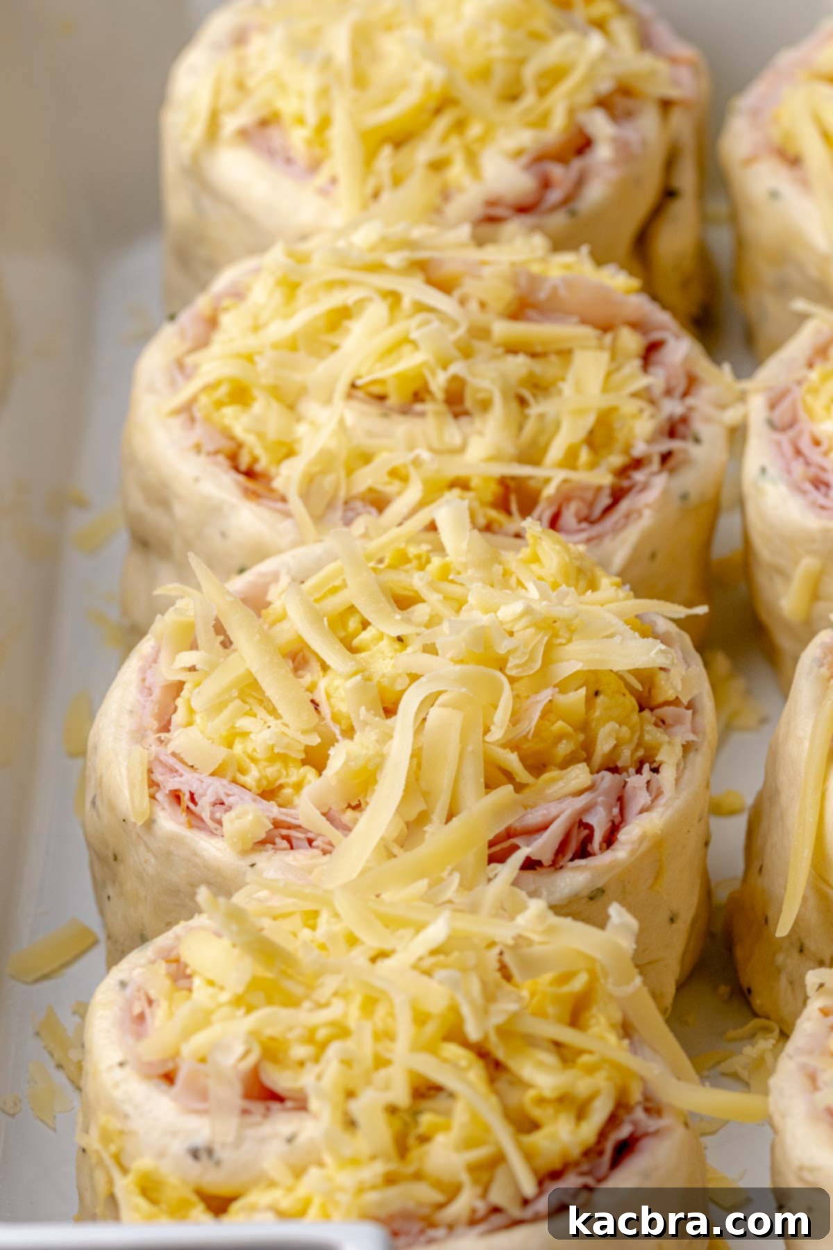 Fluffy Savory Rolls with Golden Hollandaise 14 Savory breakfast rolls topped with additional shredded cheese in a casserole dish, ready to bake.