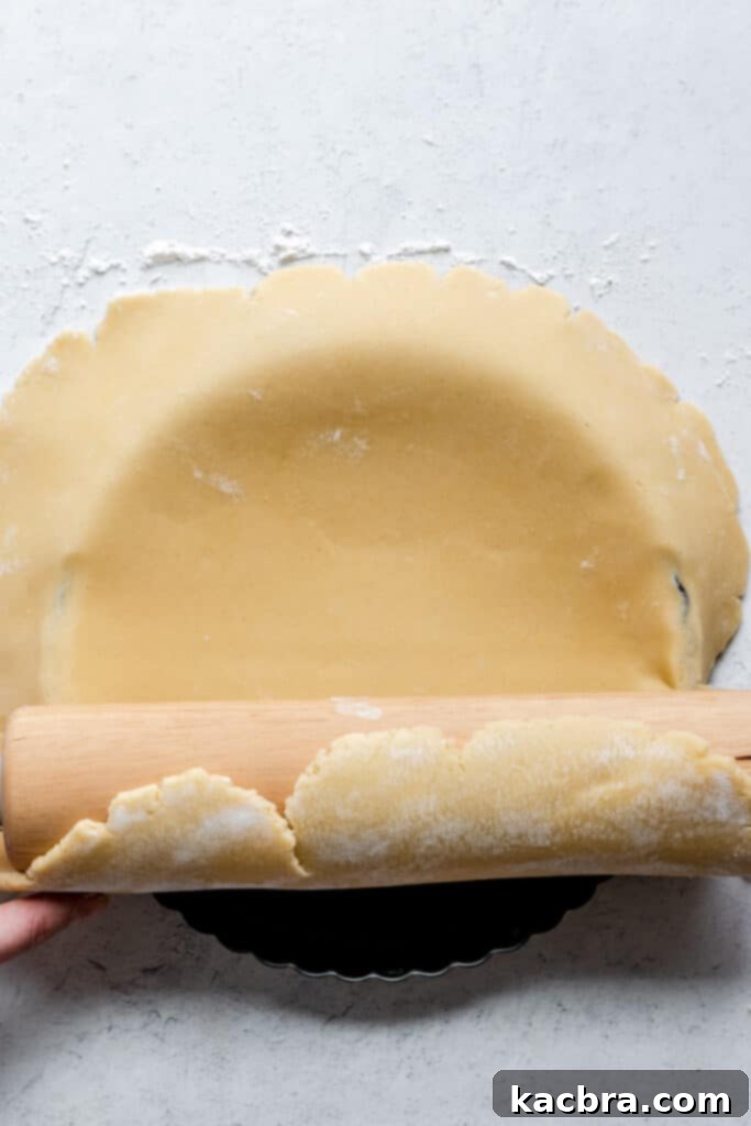 Pressing the dough into the bottom and sides of the tart pan with fingers, ensuring no air pockets.