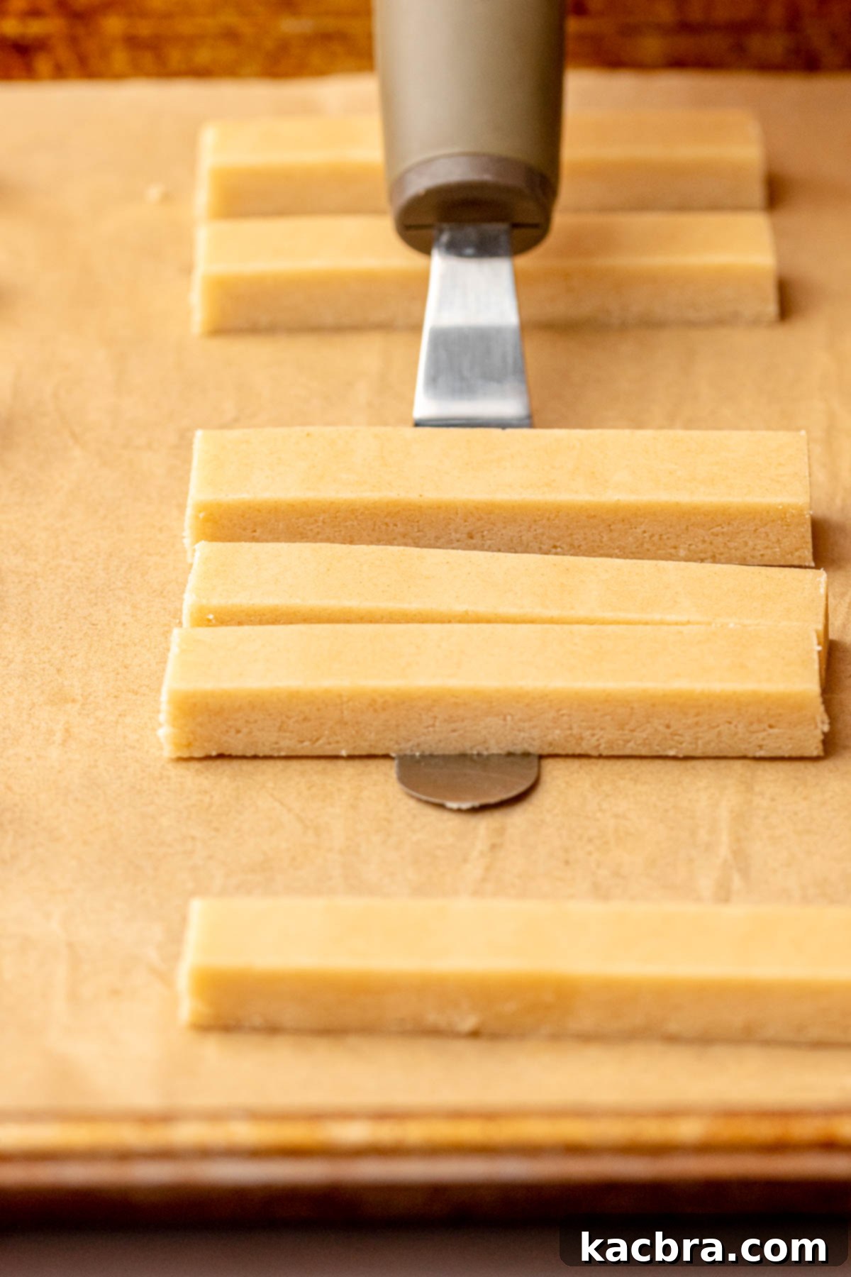 Irresistible Chocolate Cookie Dippers 13 An offset spatula gently picks up a cookie stick to transfer it onto a parchment-lined baking pan.