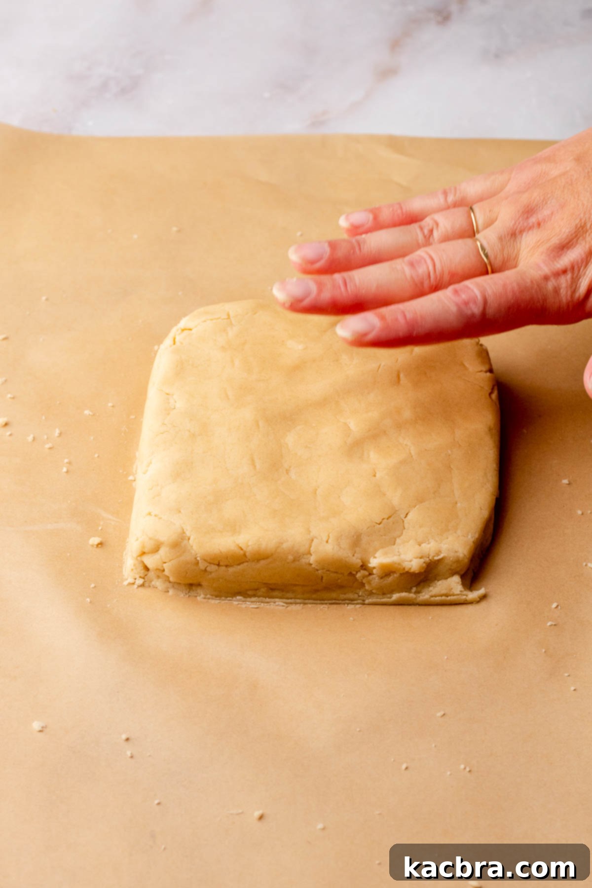 Chocolate Coated Cookie Wands 9 A hand presses shortbread dough into a rough square shape on parchment paper.