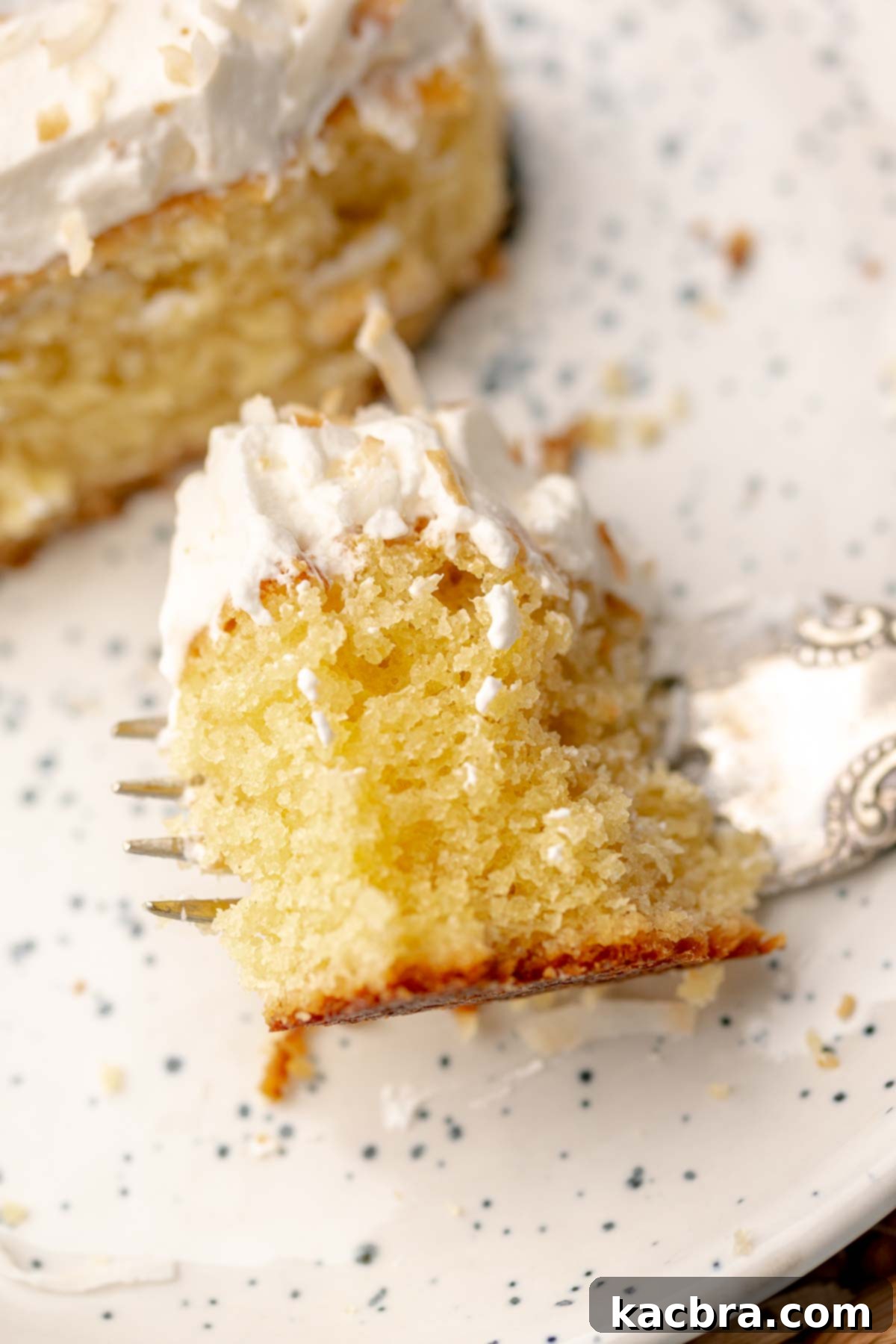 A piece of coconut almond cake on a fork, showing its moist interior and topping.
