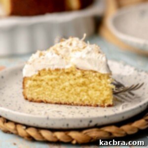 A slice of coconut almond cake on a plate with a fork next to it.