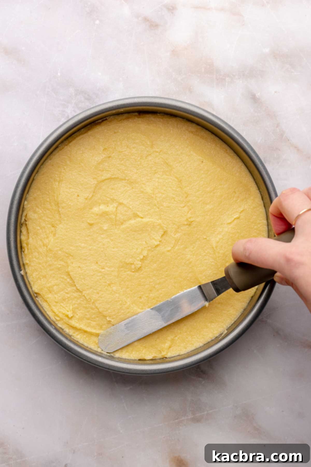 A spatula smoothing out almond cake batter in a prepared pan.