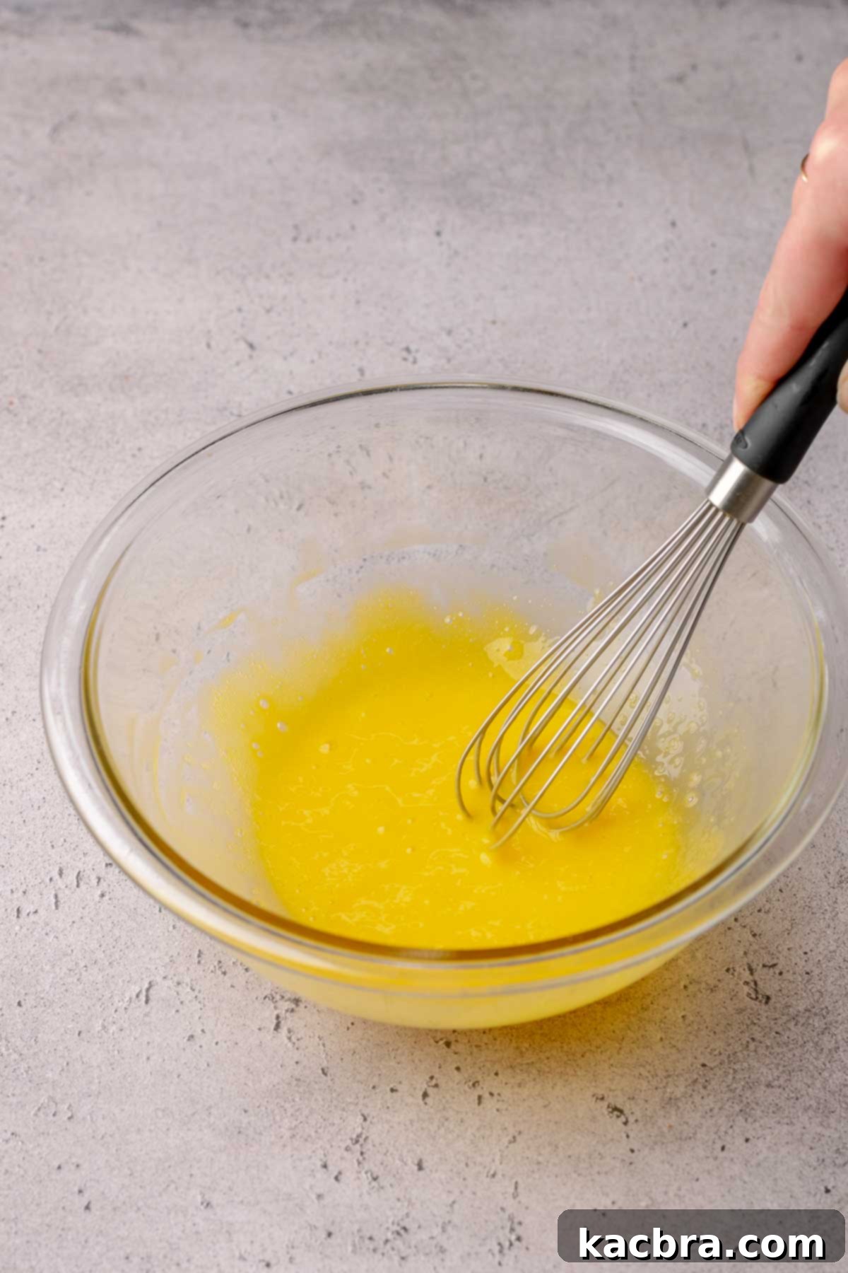 A hand whisks egg yolks in a bowl.