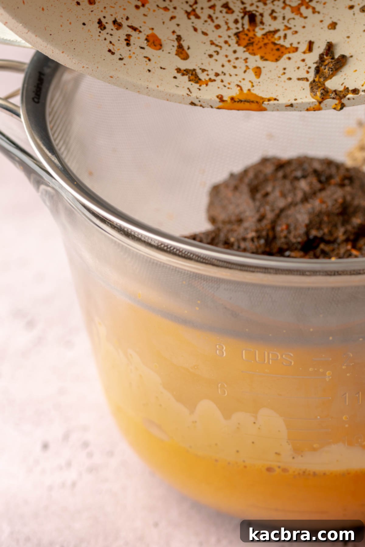 Steeped thai tea in a fine mesh sieve on top of a bowl.