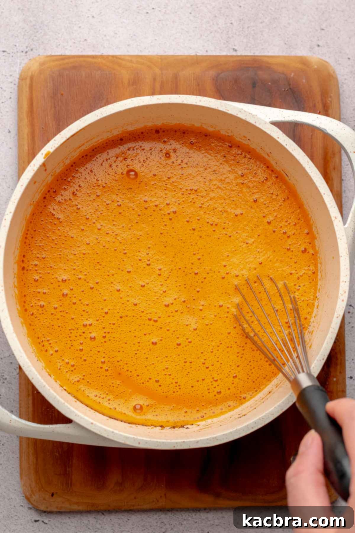 A whisk mixes thai tea custard in a saucepan.