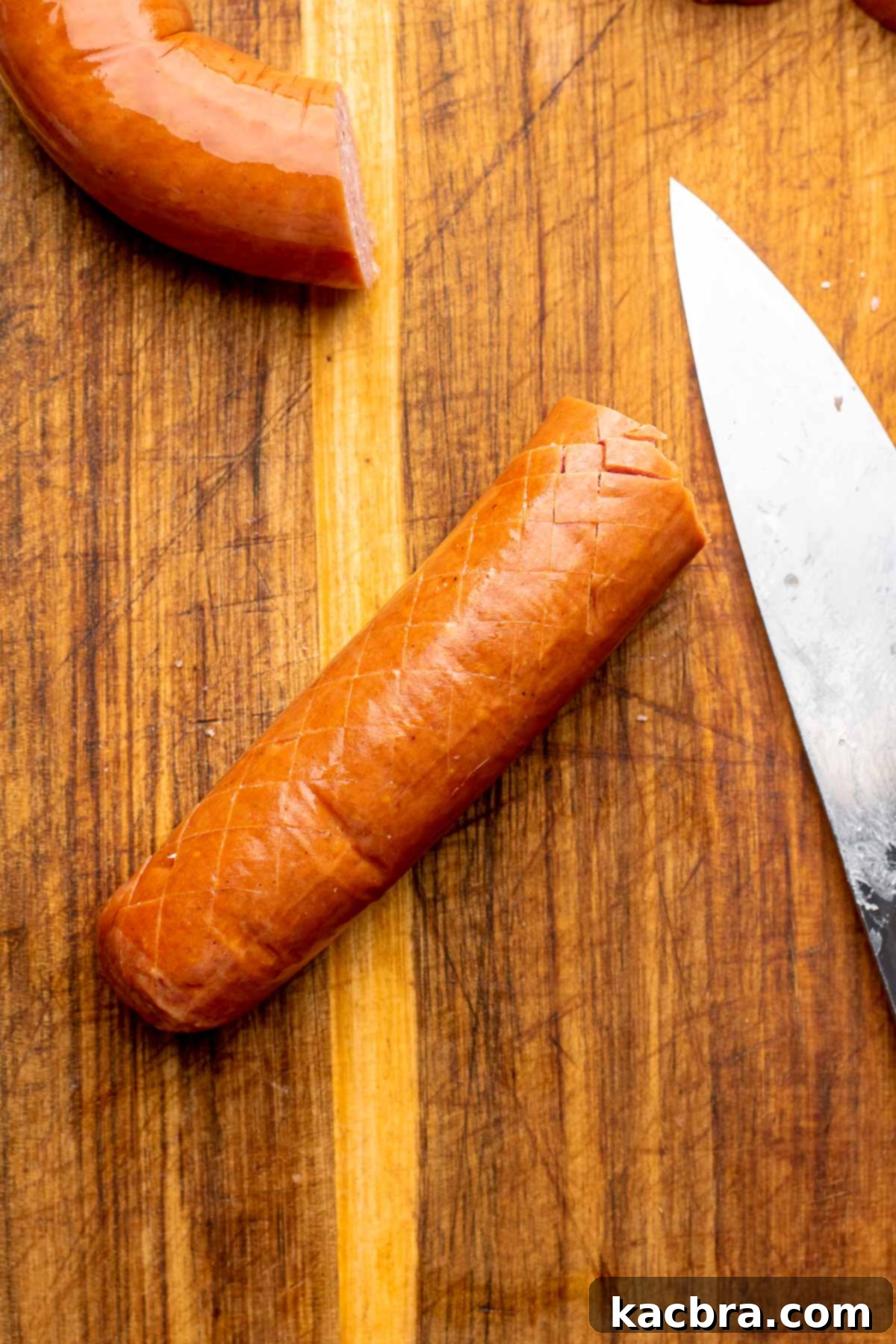 A cross hatched piece of kielbasa on a cutting board.