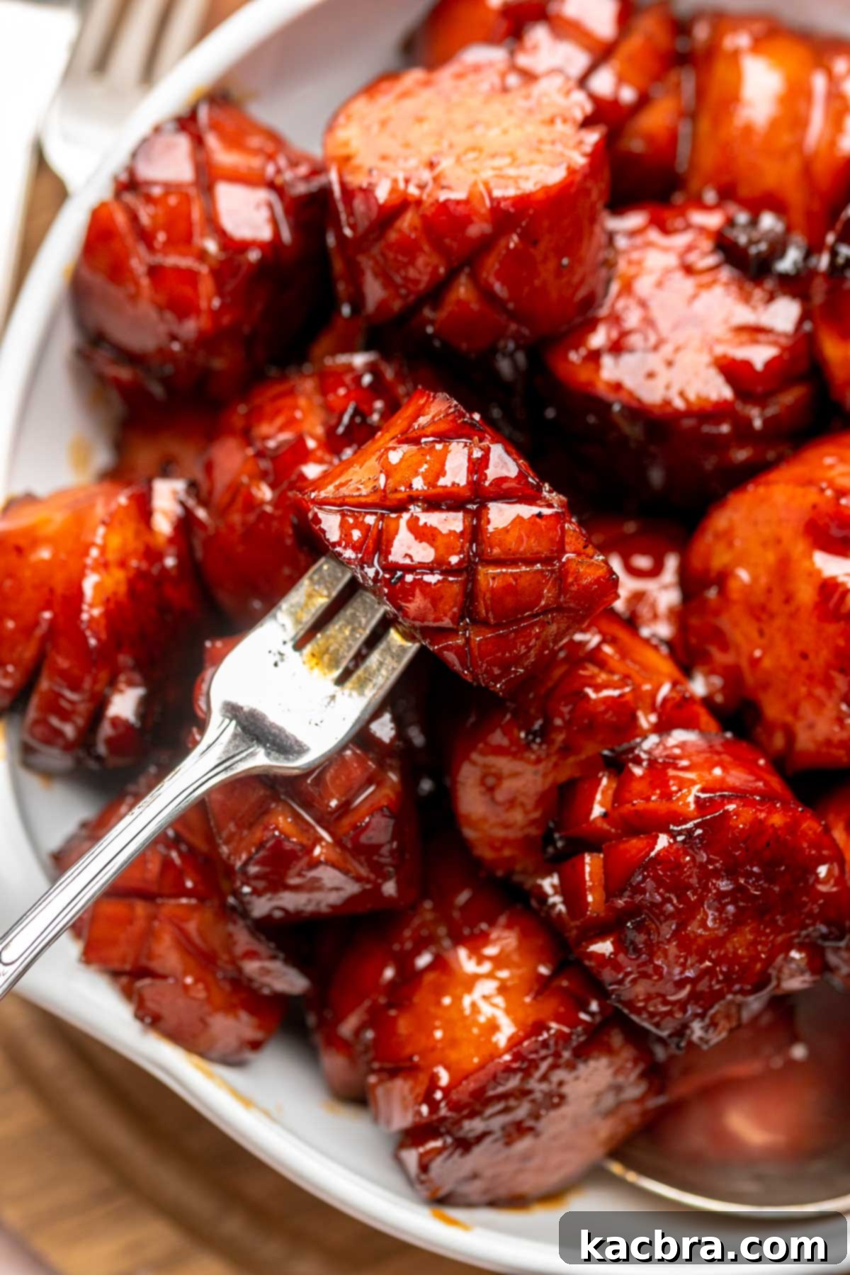 A fork holds a chunk of kielbasa in a bowl of other pieces.