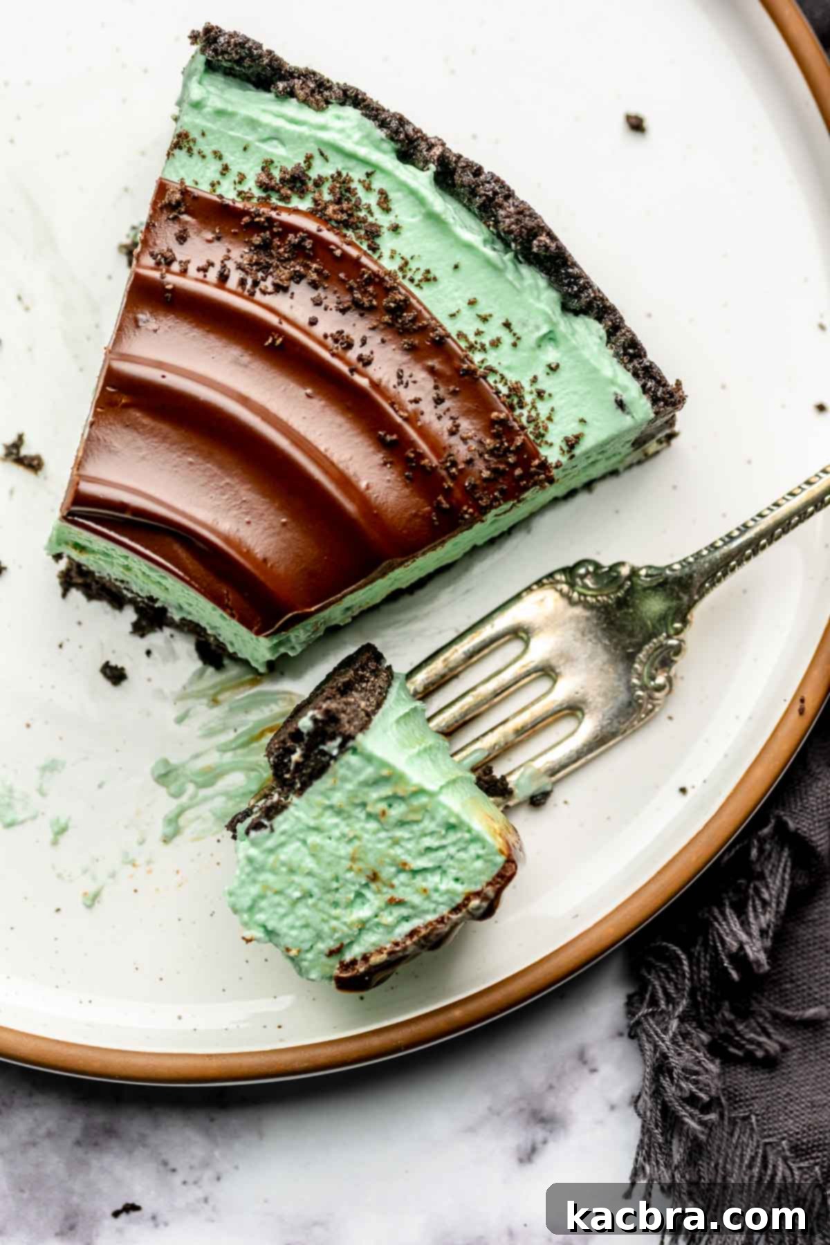 A slice of mint pie on a plate with a bite removed sitting on a fork.