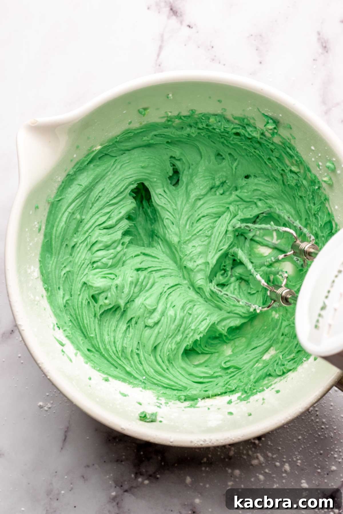 A hand mixer mixes green mint pie filling in a bowl.