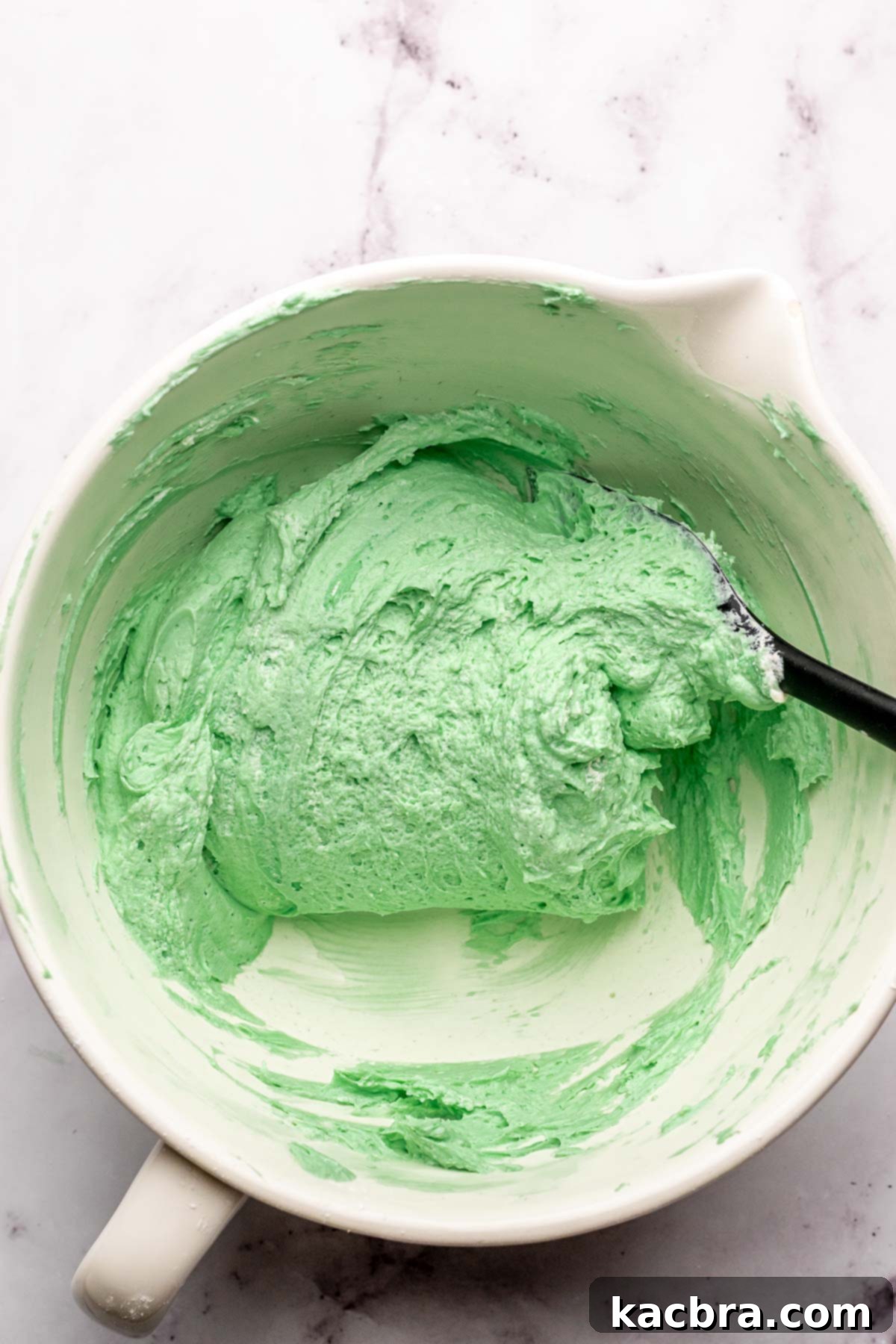 A rubber spatula folds whipped cream into mint pie filling in a bowl.
