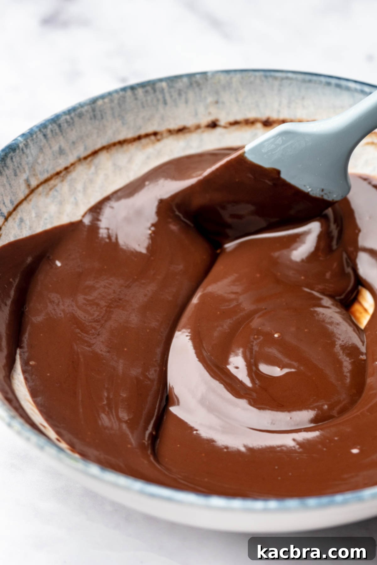 A spatula mixes chocolate ganache in a bowl.