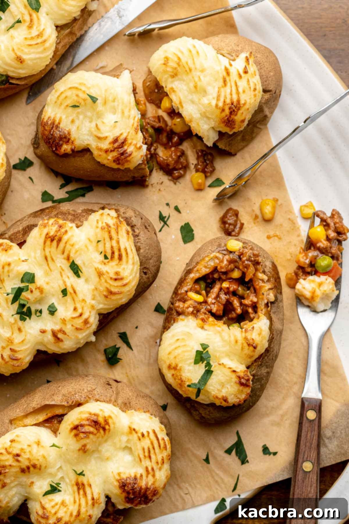 Meat stuffed potatoes on a platter. One is cut open and one has a bite removed.