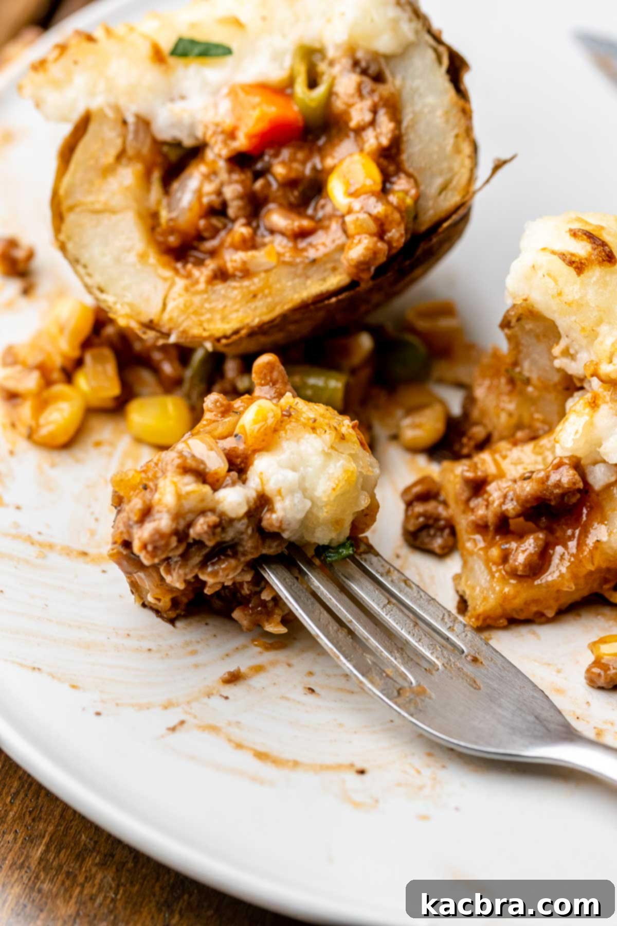 Cut open beef stuffed potato on a plate with a fork holding filling.
