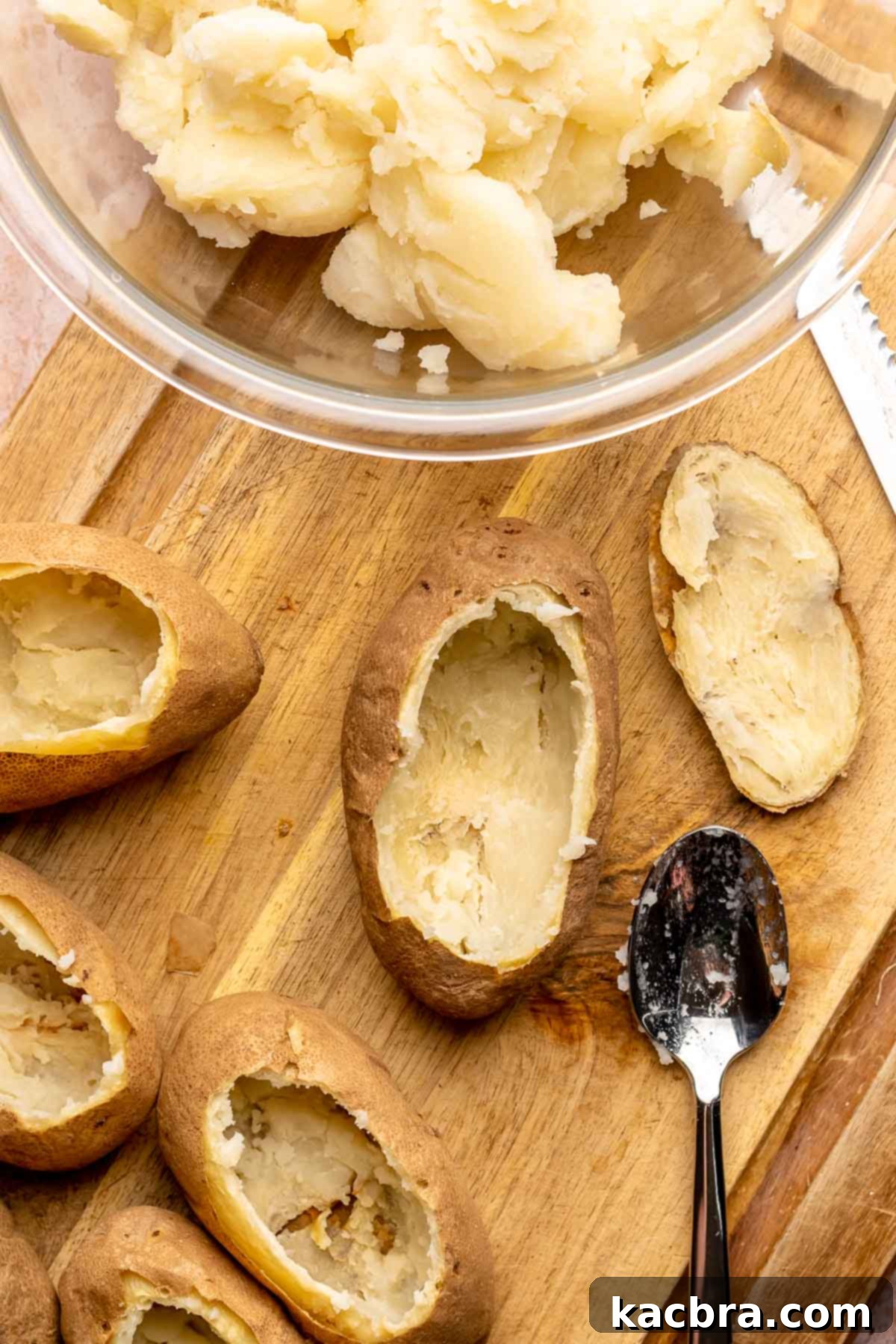 Scooped out baked potatoes on a cutting board with a spoon and bowl.