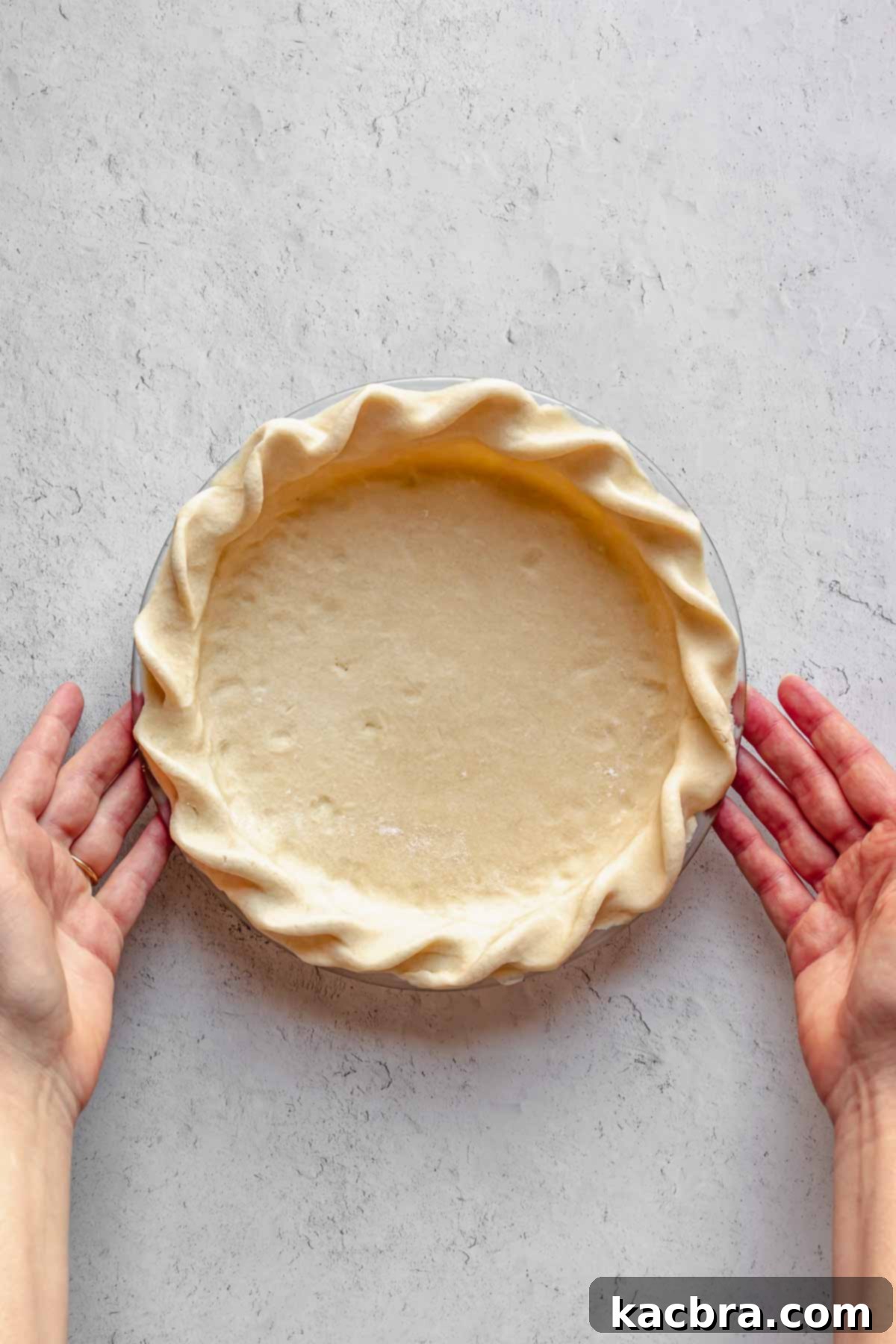 Hands delicately hold a beautifully crimped, golden-brown pie crust, showcasing its perfect texture and artisanal finish.