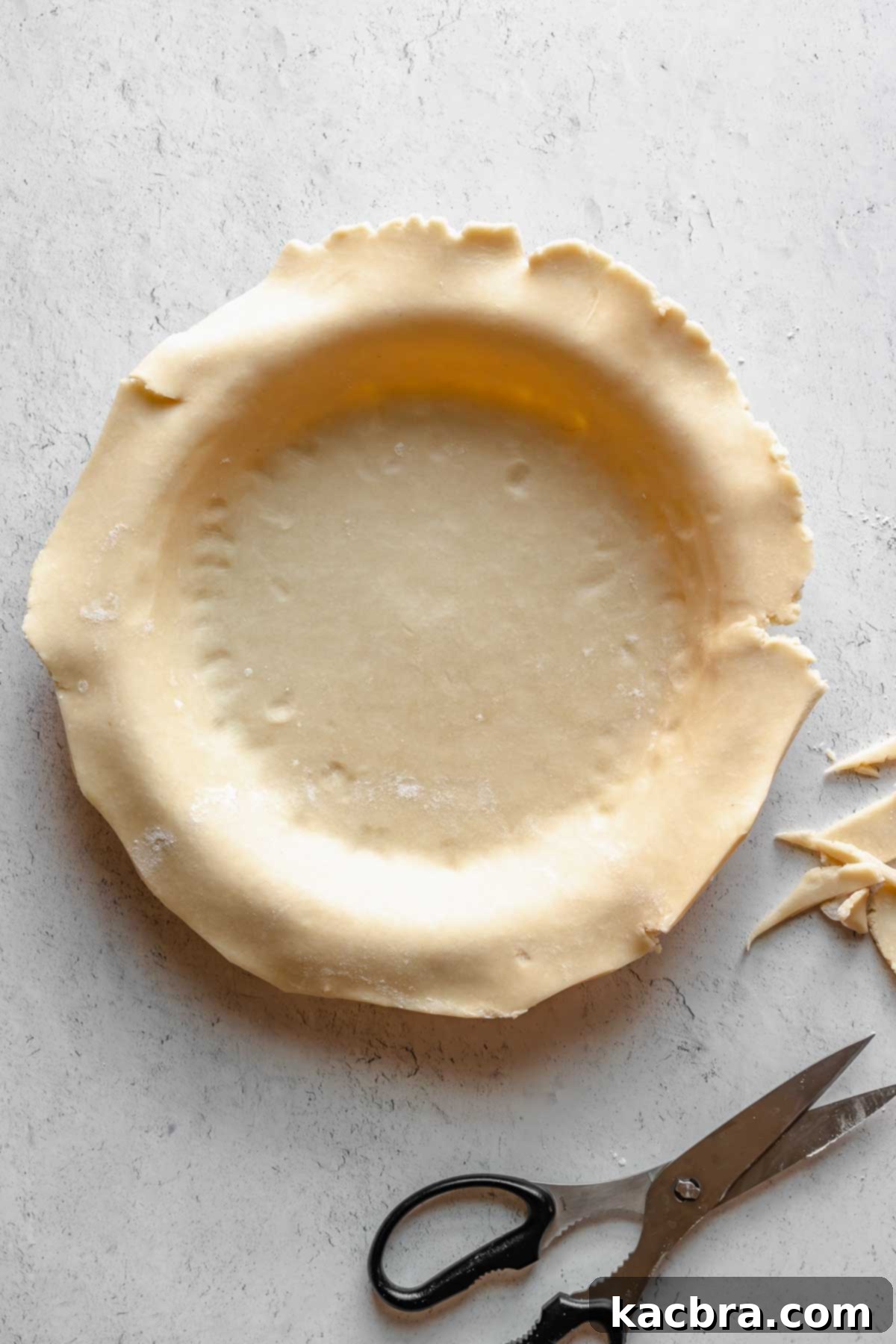 Perfectly Flaky All-Butter Crust 11 Scissors trimming the edges of pie dough in a pie plate.