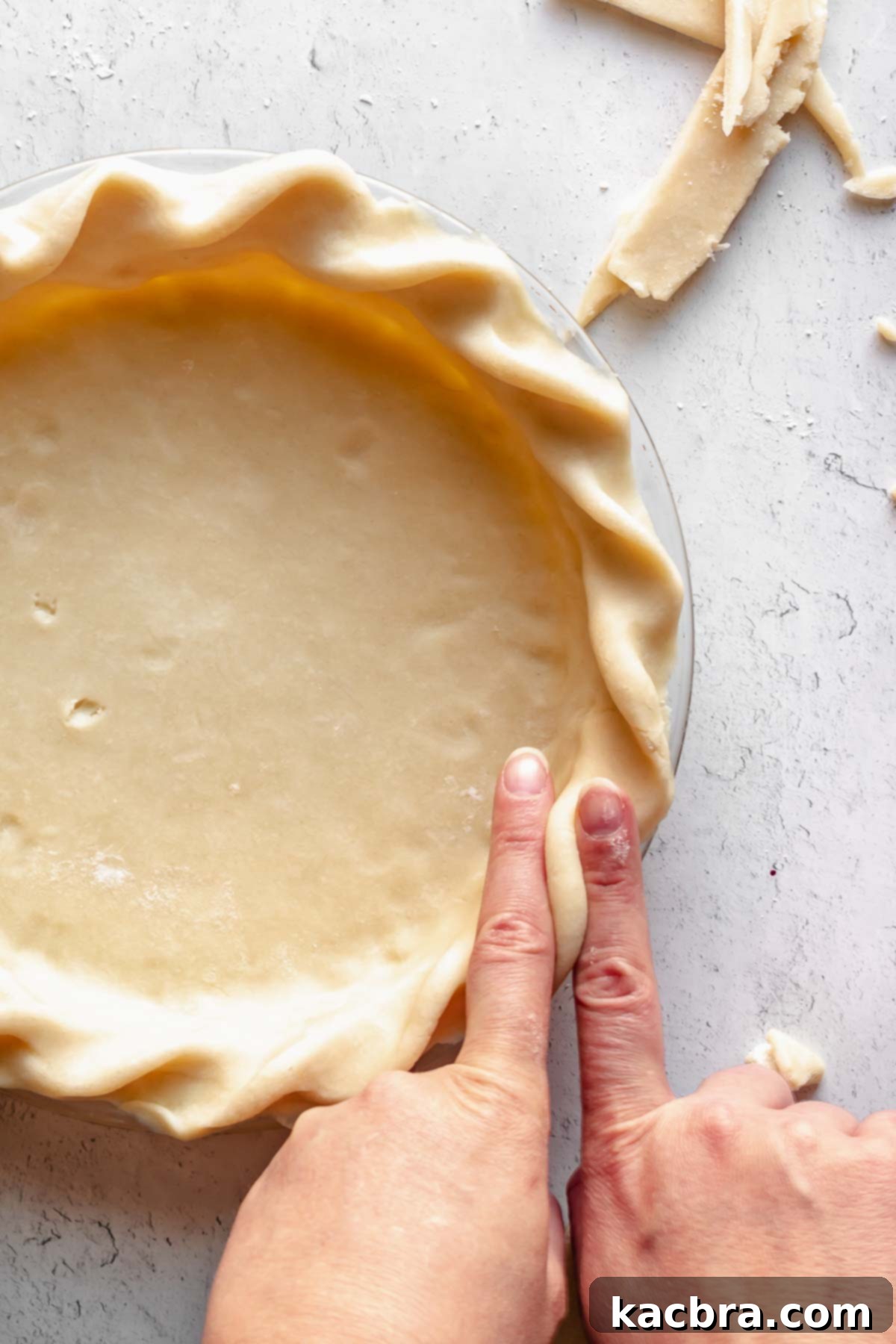 Fingers expertly crimping the edges of a pie dough into a decorative pattern, preparing it for baking.