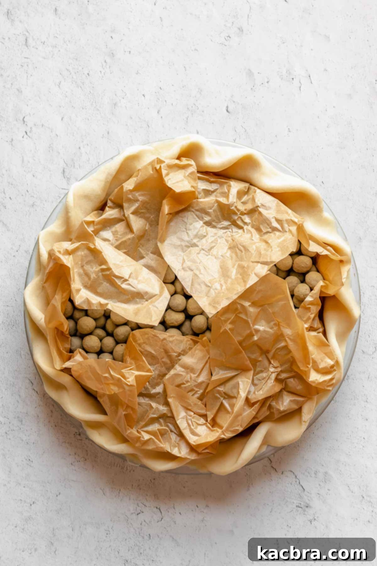 Parchment paper and pie weights inside a pie crust, with the parchment folded inwards to protect the crimped edges from over-browning.